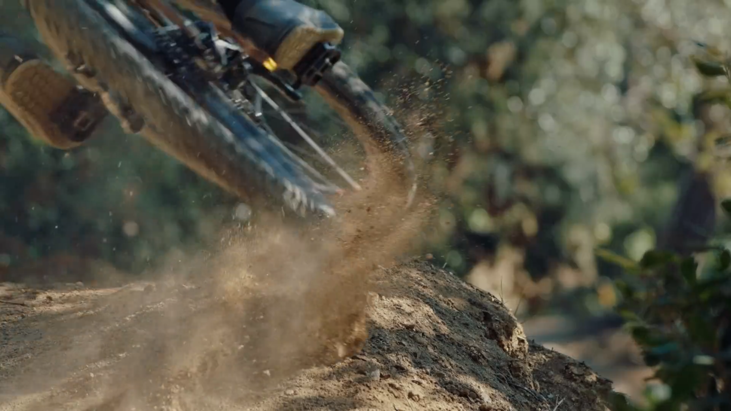 Nahaufnahme eines Rasentraktors, der auf unebenem Boden fährt, Staub aufwirbelt, im Hintergrund Bäume.