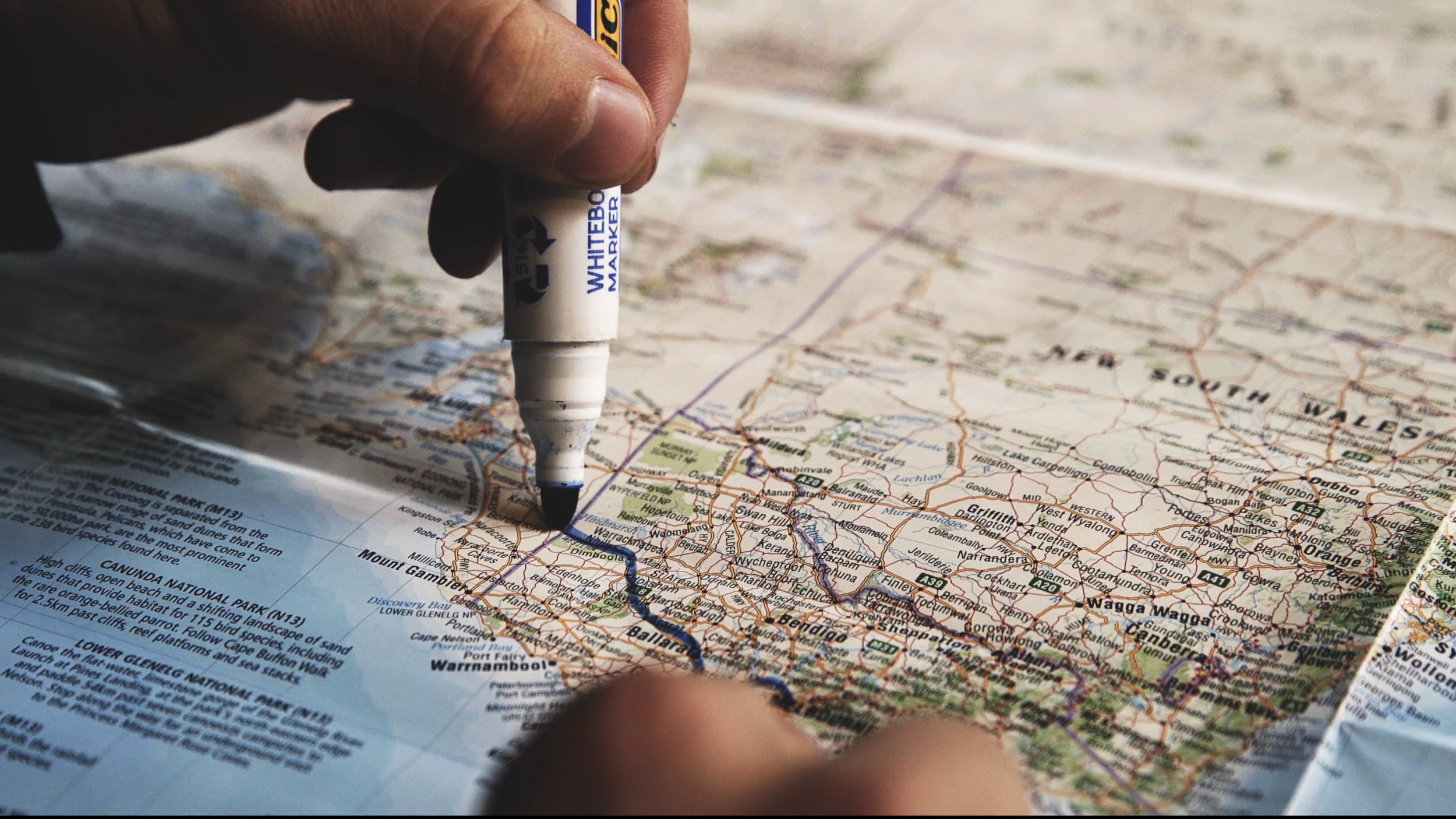 Nahaufnahme einer Hand, die mit einem weißen Marker auf einer Landkarte zeichnet, die sich auf Australien konzentriert zeigt.