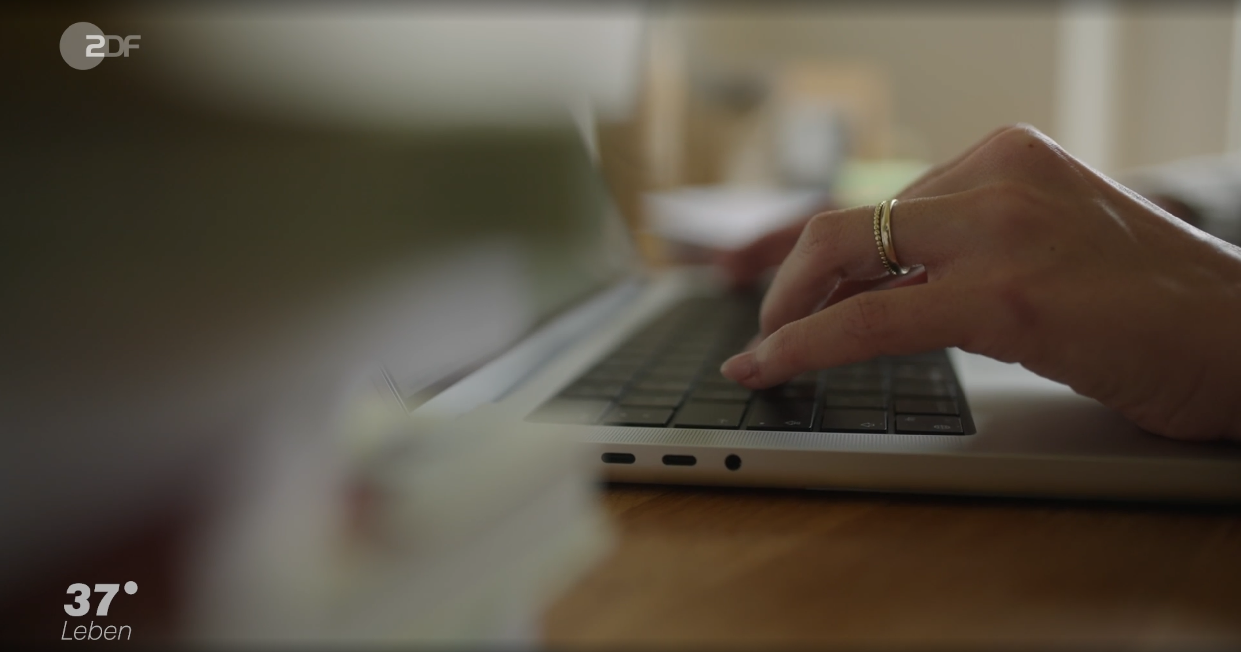 Nahaufnahme einer Hand, die auf einer Laptop-Tastatur tippt, im Hintergrund unscharf. Ein Ring ist an einem Finger sichtbar.
