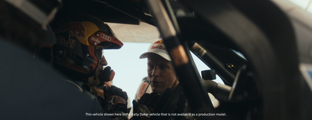 Zwei Männer im Gespräch im Innenraum eines Rallye-Fahrzeugs, eines trägt einen Helm und die andere eine Basecap mit Red Bull Logo.