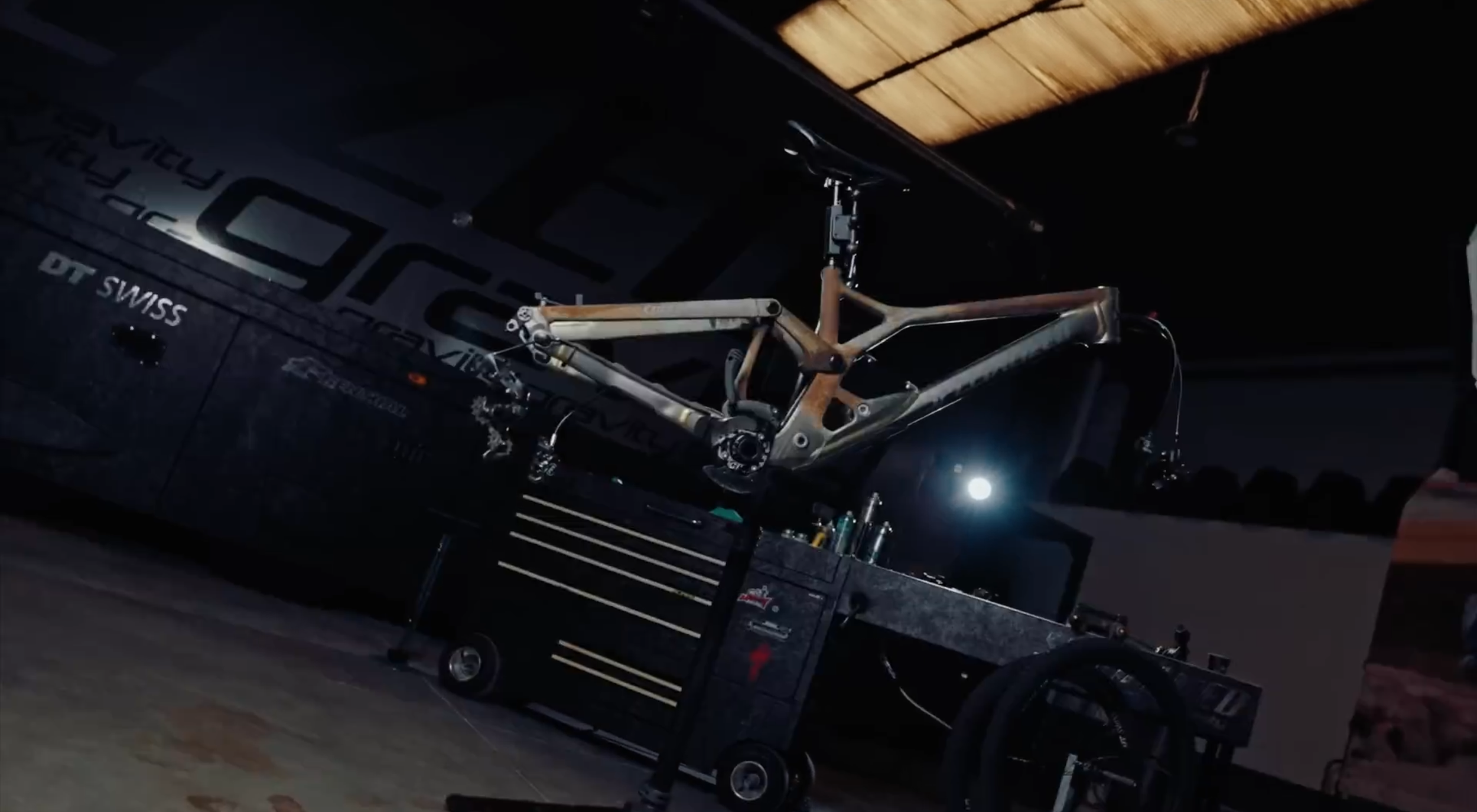 Leeres Fahrradrahmen in einer Werkstatt auf einem Werkstattwagen, im Hintergrund Werkzeug und eine dunkle Wand mit Schriftzug.