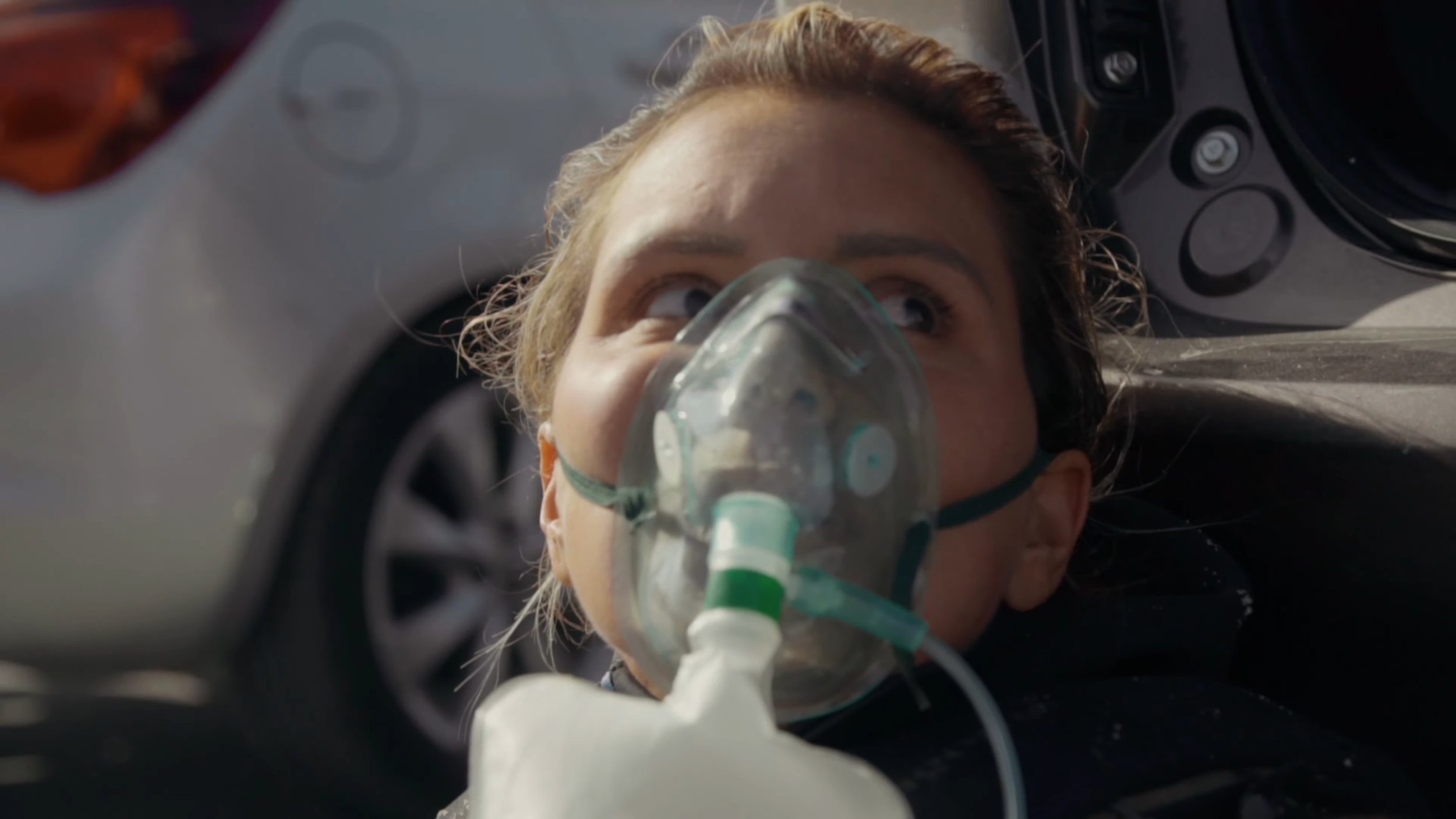 Eine Frau mit Sauerstoffmaske liegt auf dem Boden neben einem Fahrzeug, Blick nach oben