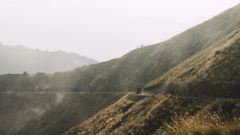 Berglandschaft mit schmaler Straße, die an steilen Hängen entlangführt, und einem Auto unterwegs.