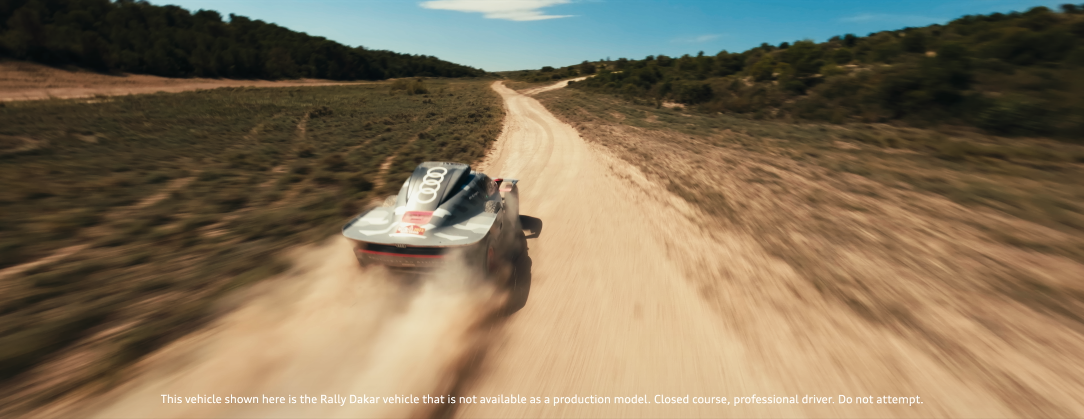 Ein Audi-Sportwagen fährt auf einer unbefestigten, kurvigen Straße durch eine ländliche, hügelige Landschaft mit Büschen und Bäumen, Staub wirbelt hinter dem Fahrzeug auf.