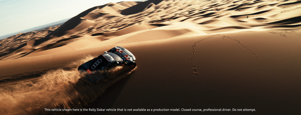 Ein Audi Rallyefahrzeug, das in der Wüste auf Sanddünen fährt, hinterlässt eine Staubspur.