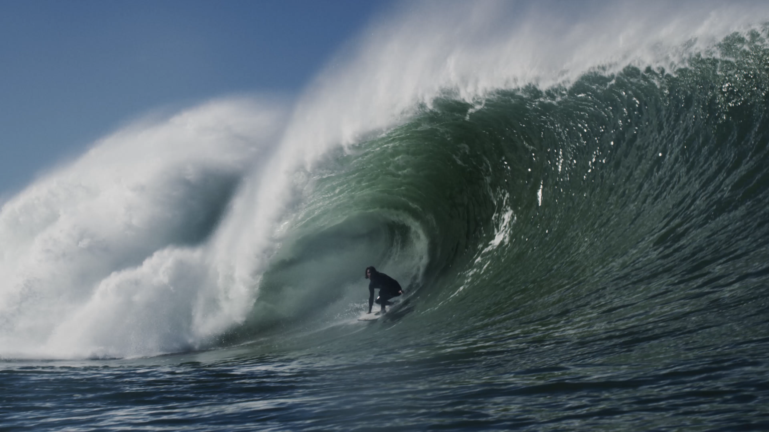 Ein Surfer auf einem Surfbrett, der durch die Innenwand einer großen Welle fährt.