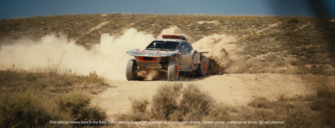 Ein umgebauter Geländewagen fährt auf einer staubigen Wüstenstraße, es entstehen Staubwolken im Rücken.