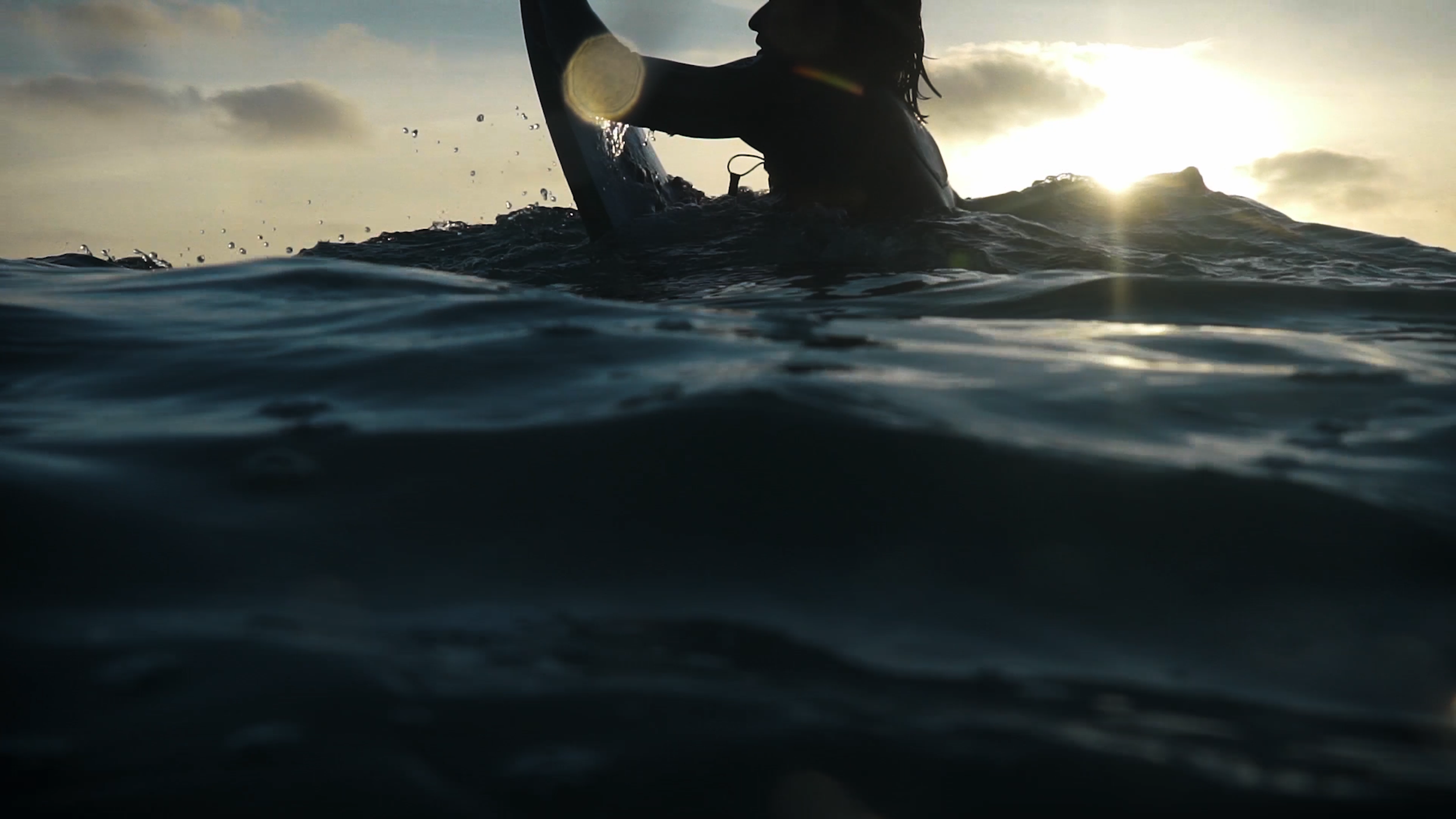 Im Wasser schwimmende Person beim Surfen bei Sonnenuntergang, mit Blick auf den Himmel und die Wasseroberfläche.
