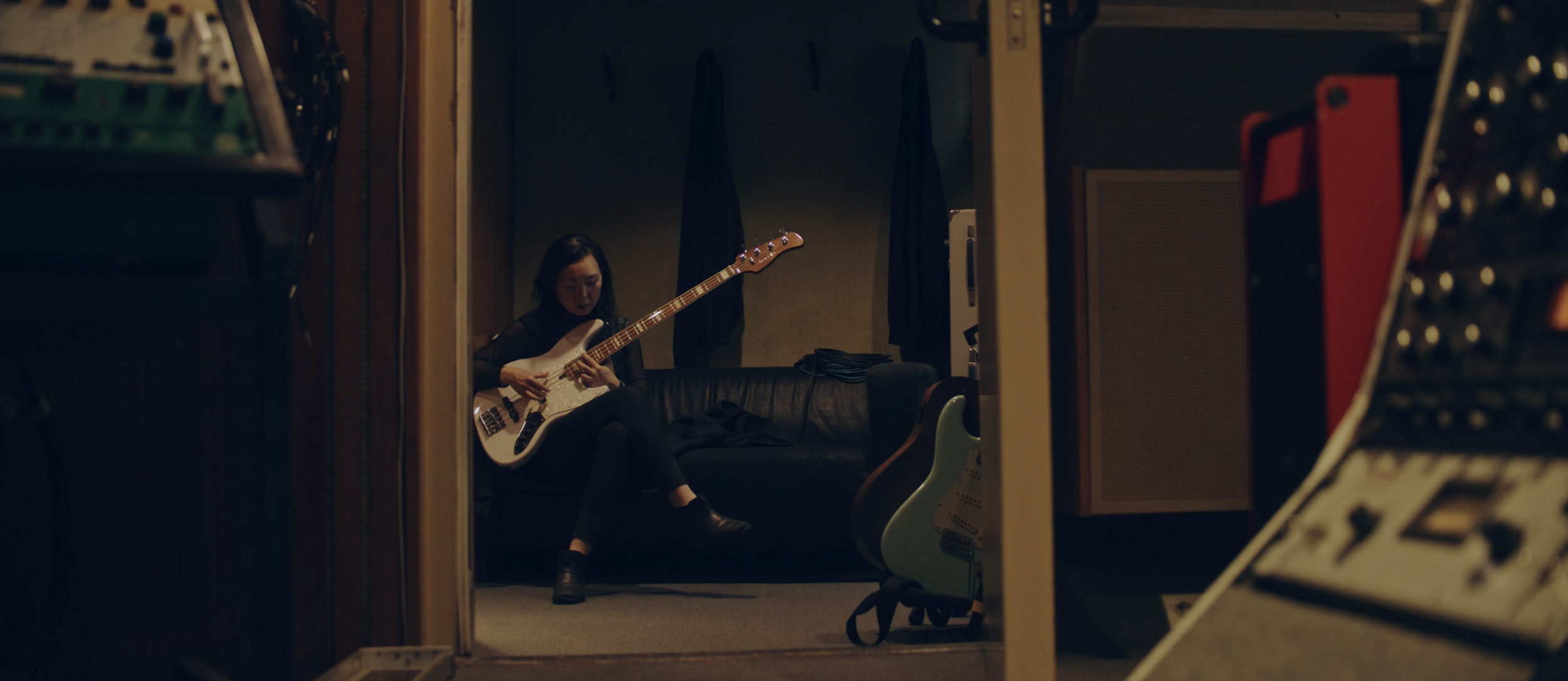 Eine Frau spielt Gitarre in einem Tonstudio, sitzend auf einem schwarzen Ledersofa.