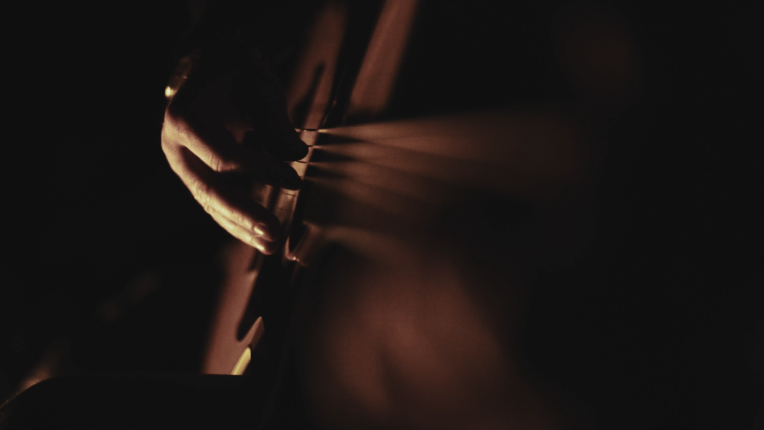 Nahaufnahme einer Hand, die eine Gitarre im dunklen Licht spielt.