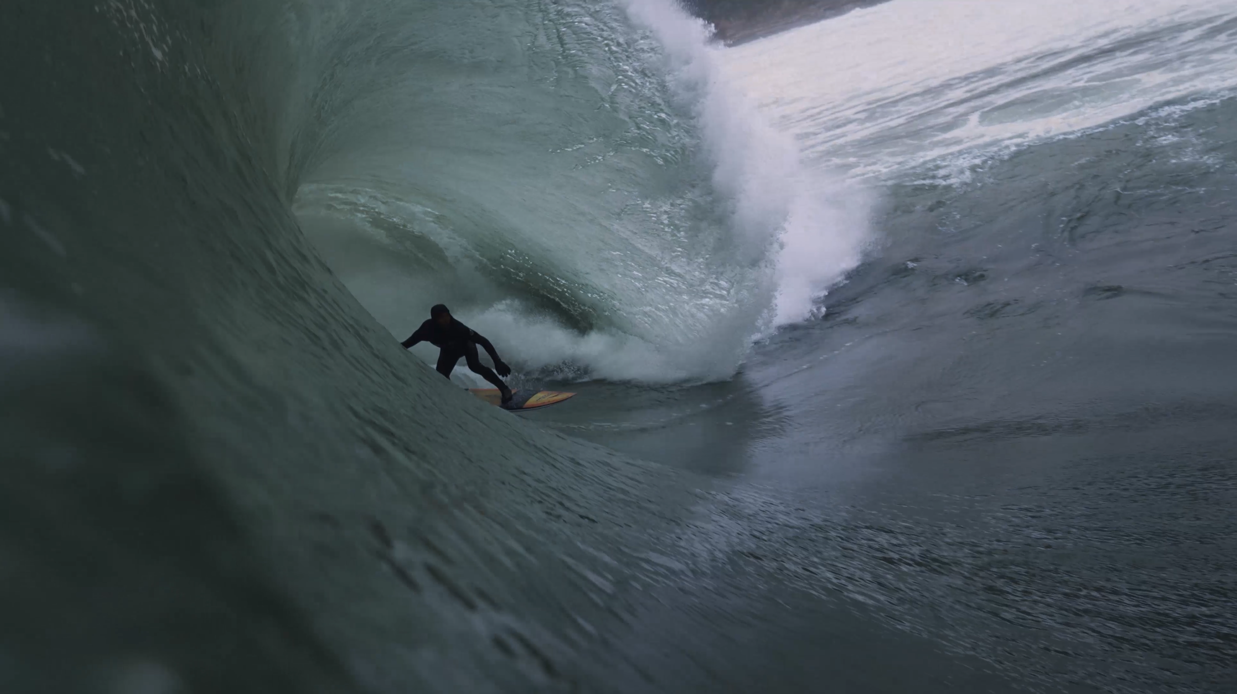 Ein Surfer in schwarzer Kleidung reitet eine große Welle im Meer.