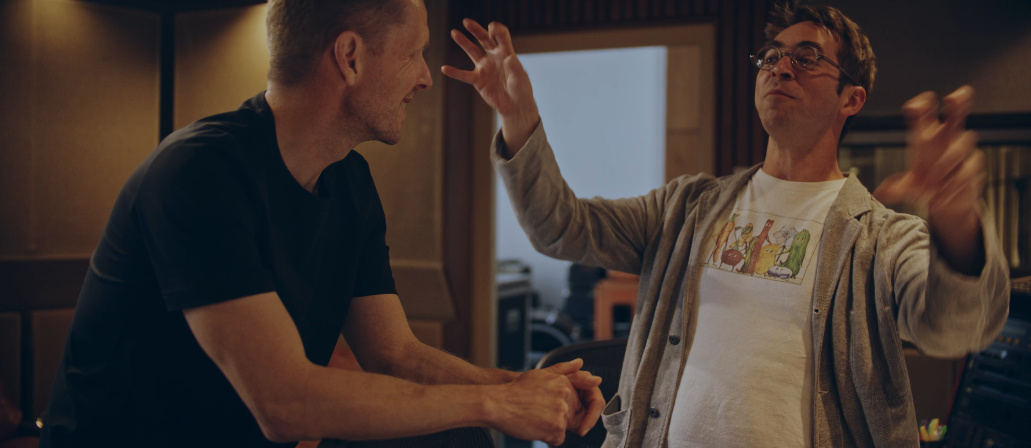 Zwei Männer in einem Raum, einer lacht und der andere gestikuliert lebhaft, vermutlich in einem Gespräch oder Streit.