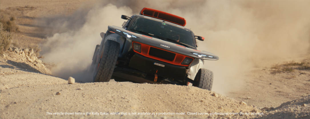 Ein Rallye-Fahrzeug fährt auf staubiger, unebener Strecke im Wüstenumfeld, wirbelt Staub auf.