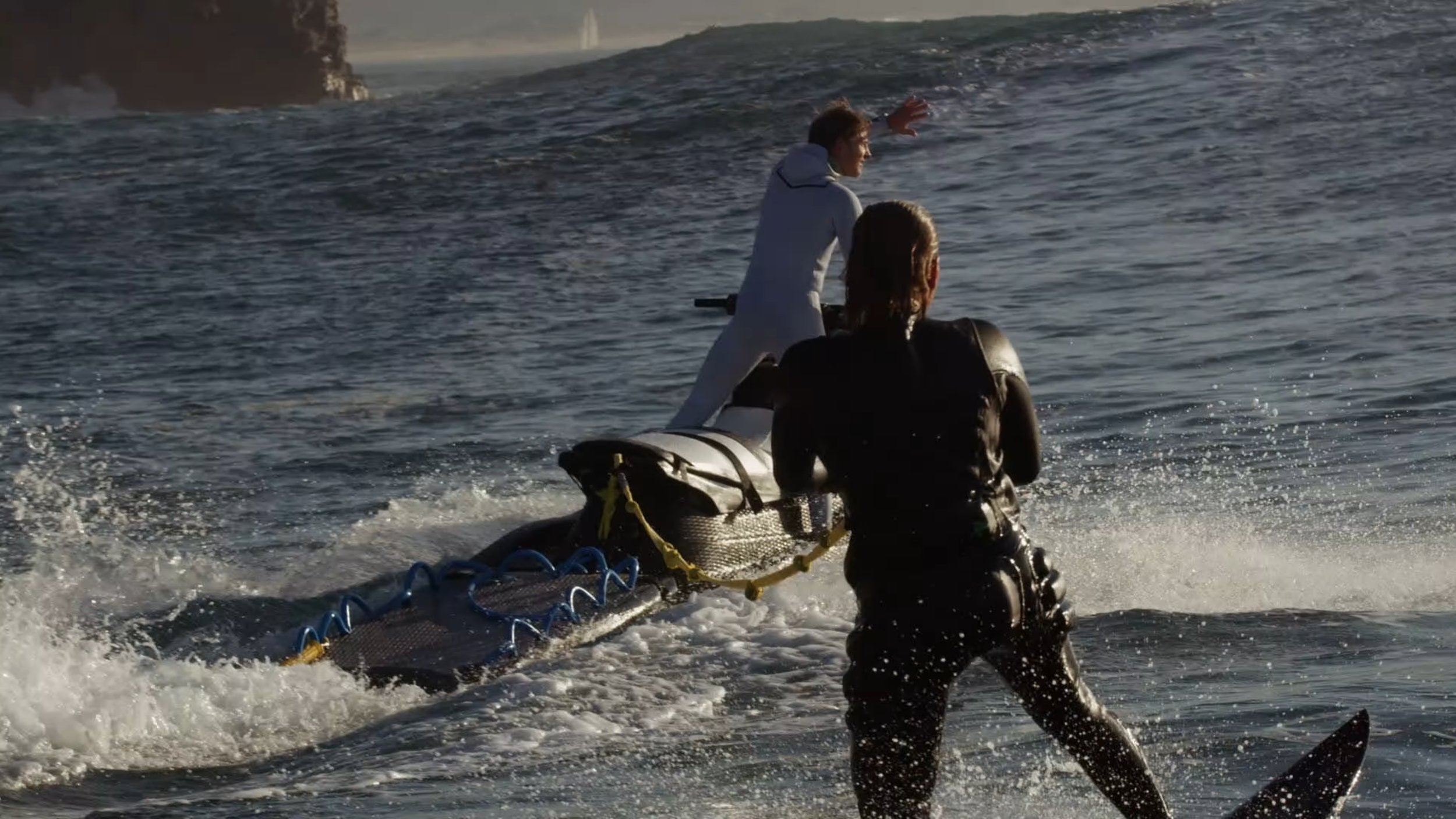 Zwei Menschen auf einem Jetski im Meer, einer sitzt auf dem Jetski, der andere läuft im Wasser und hält den Jetski fest.