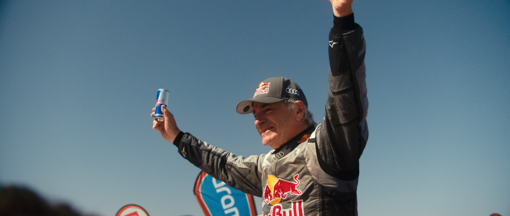 Motorsportfahrer mit Red Bull Logo, feiert mit ausgestreckten Armen gegen blauen Himmel