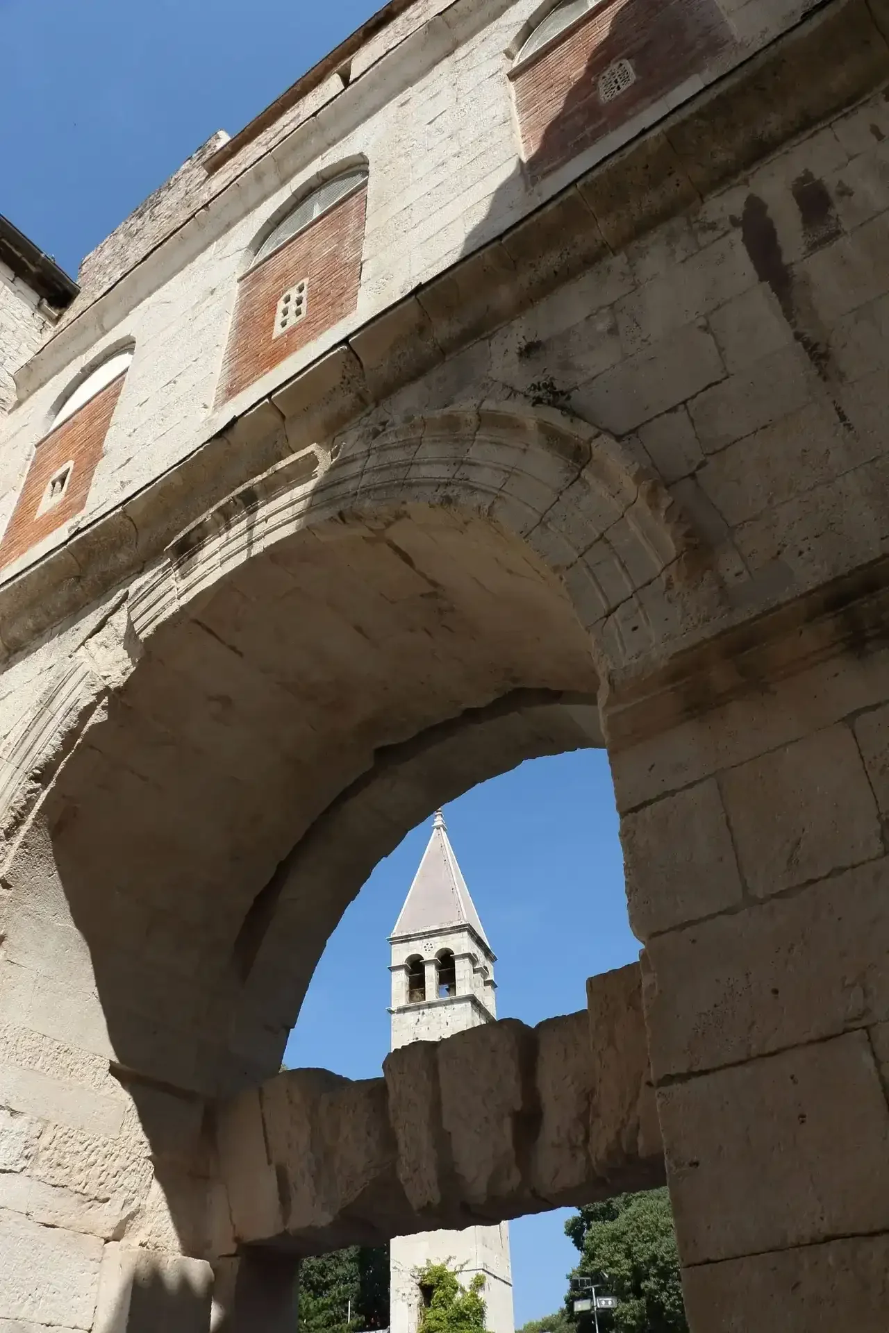 Stone archway inside Diocletian’s Palace in Split, Croatia, framing the bell tower of Saint Domnius Cathedral against a clear blue sky.