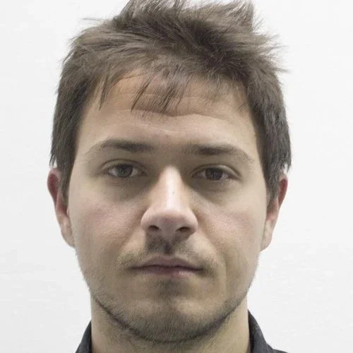A young man with short, tousled brown hair and a serious expression, looking directly at the camera.