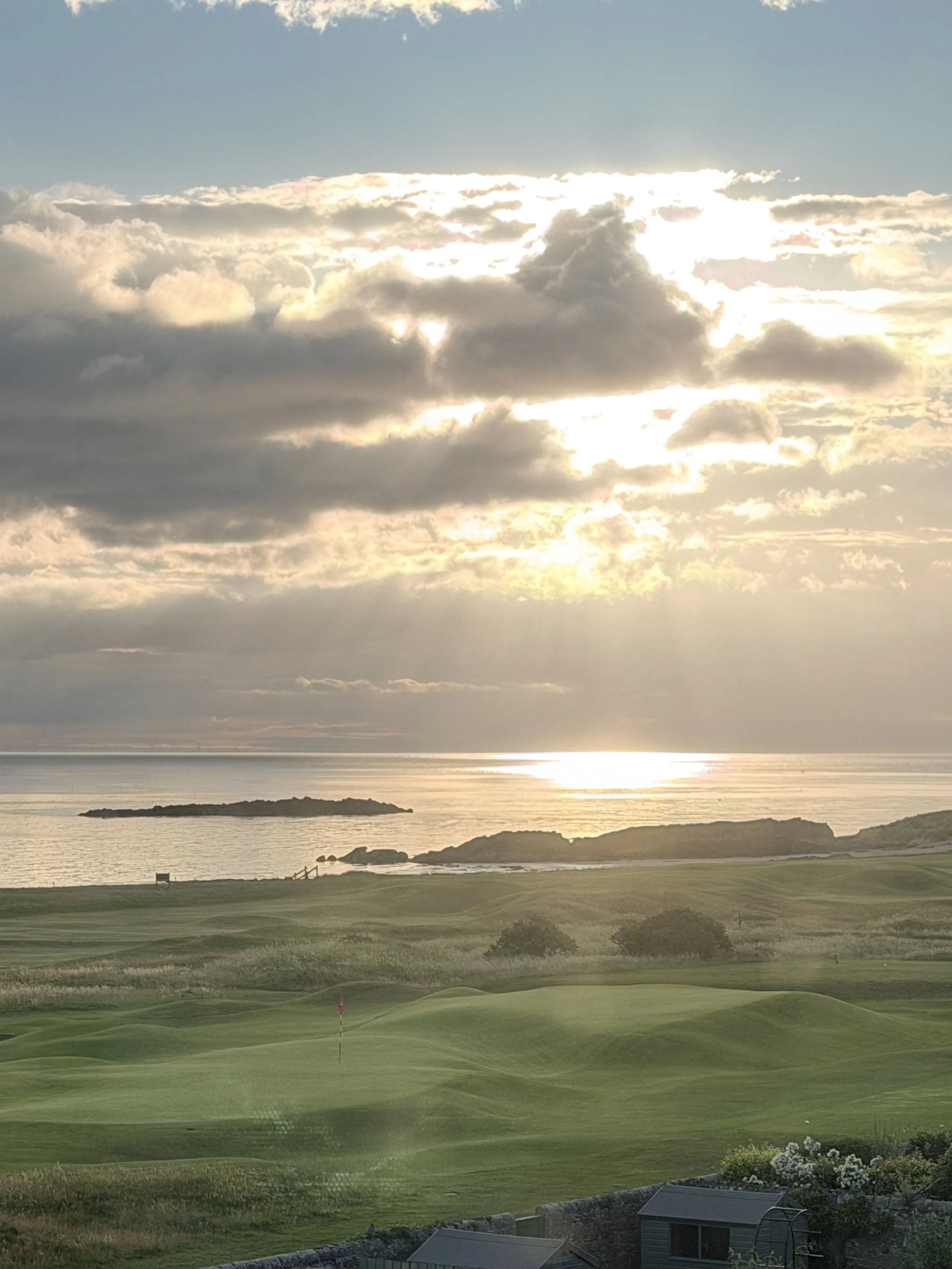 Sunset over a body of water with grassy fields, small islands, and a partly cloudy sky.