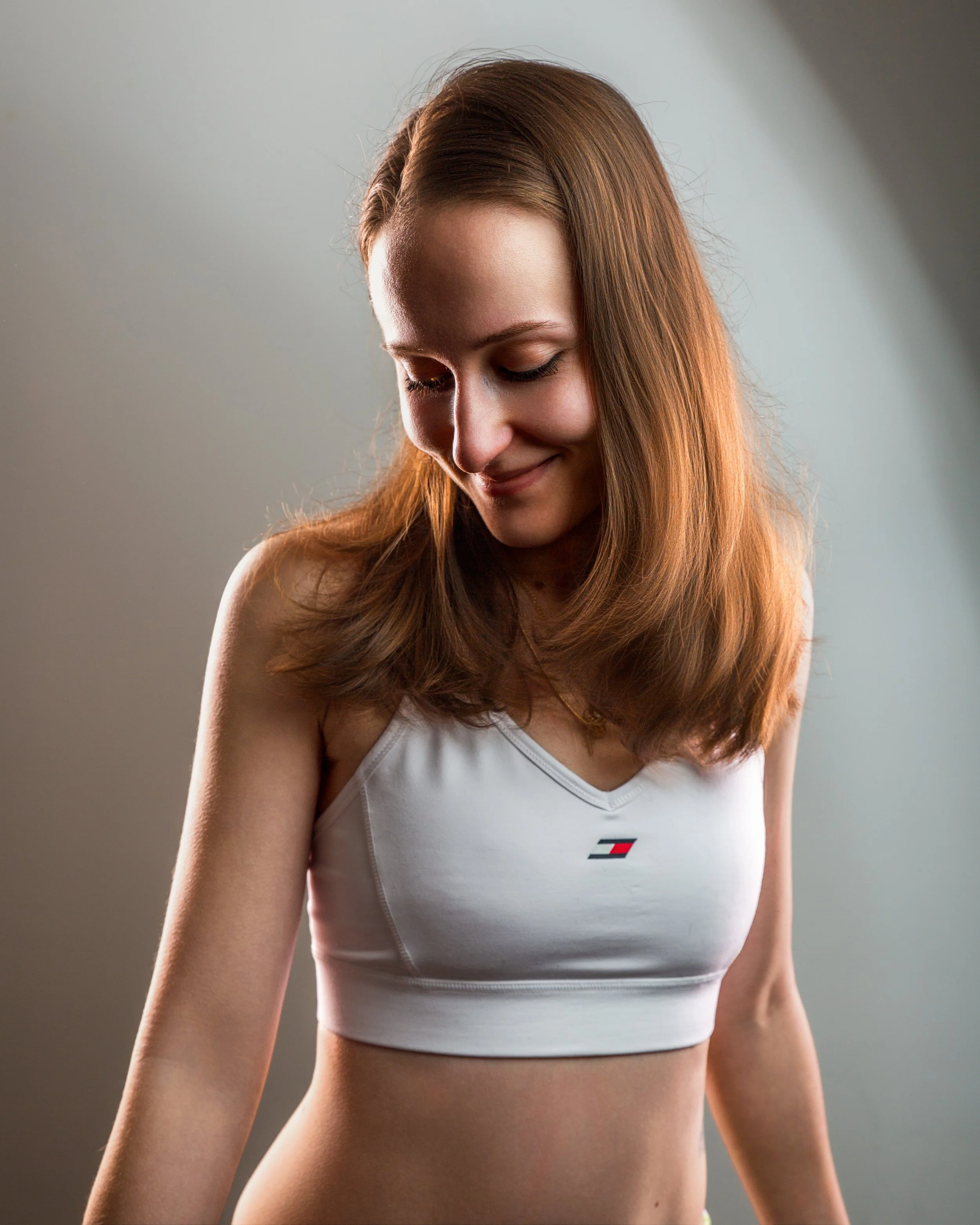 Indoor portrait of a woman the harsh Edge lighting read soft key light in front of a gradient background. She's wearing a white crop top