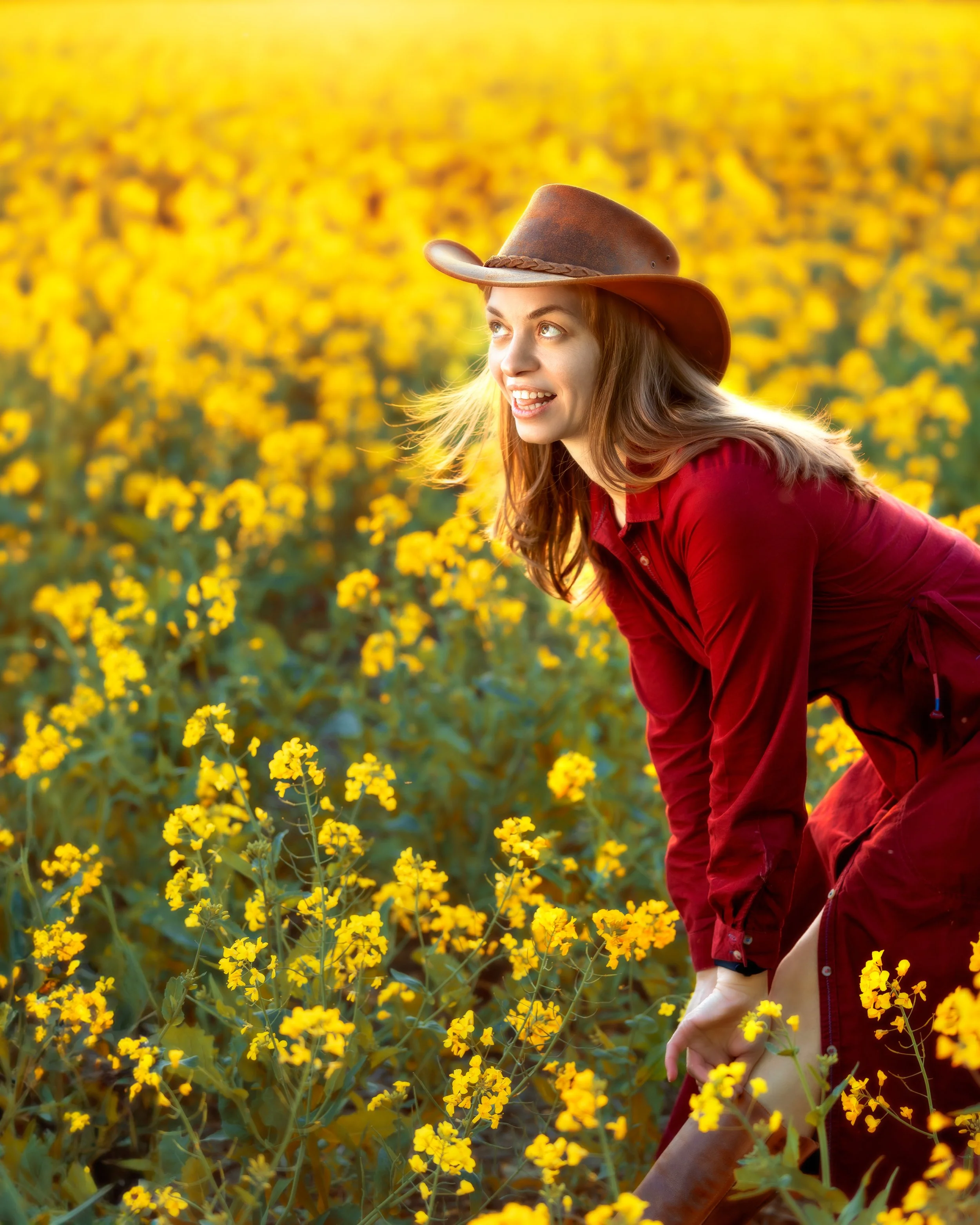 Portrait of a woman on a rape seed field, wearing a Red Dress and a cowboy hat in the sunset