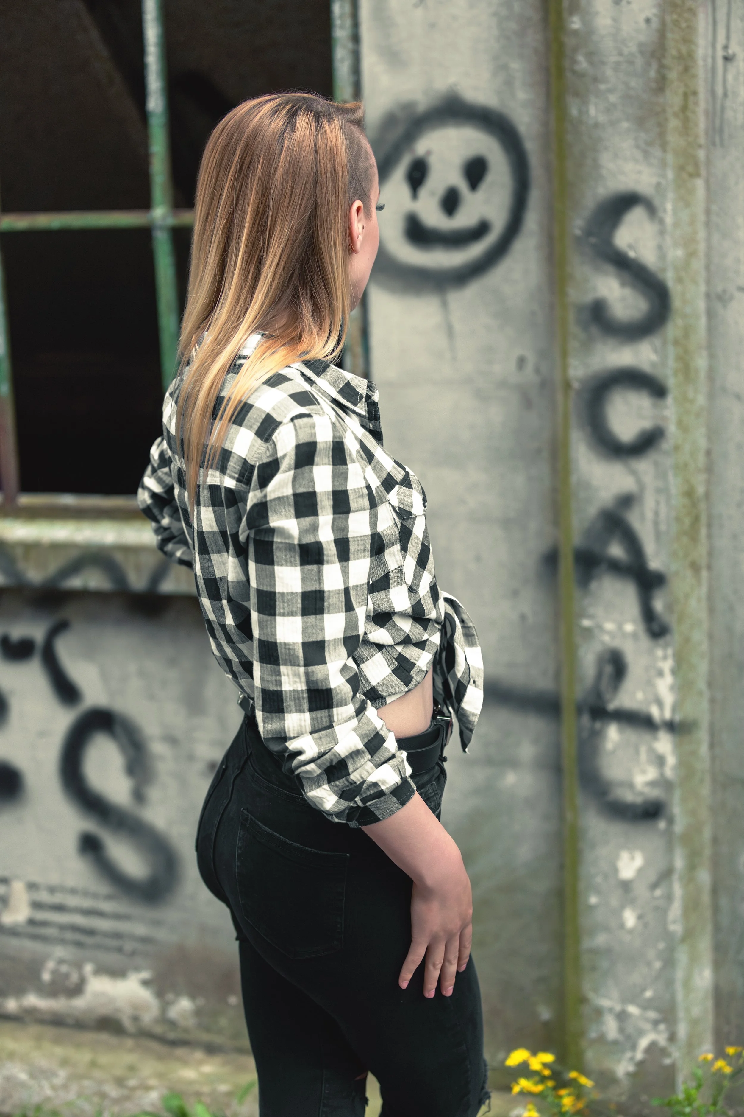 Faceless portrait of a fit blonde girl staring at smiling smiley graffiti on a concrete wall with metal window frame