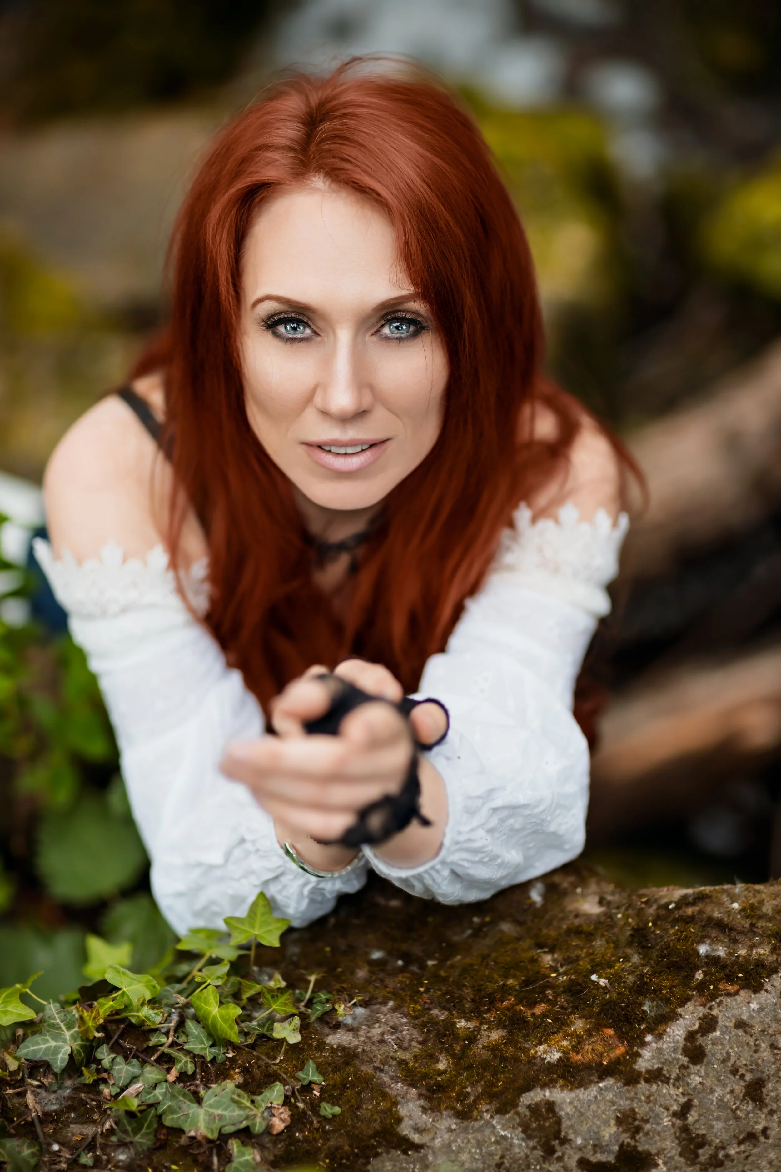 Stylised portrait of a red haired woman wearing vintage white corset and lace gloves by a waterfall in Cheltenham 