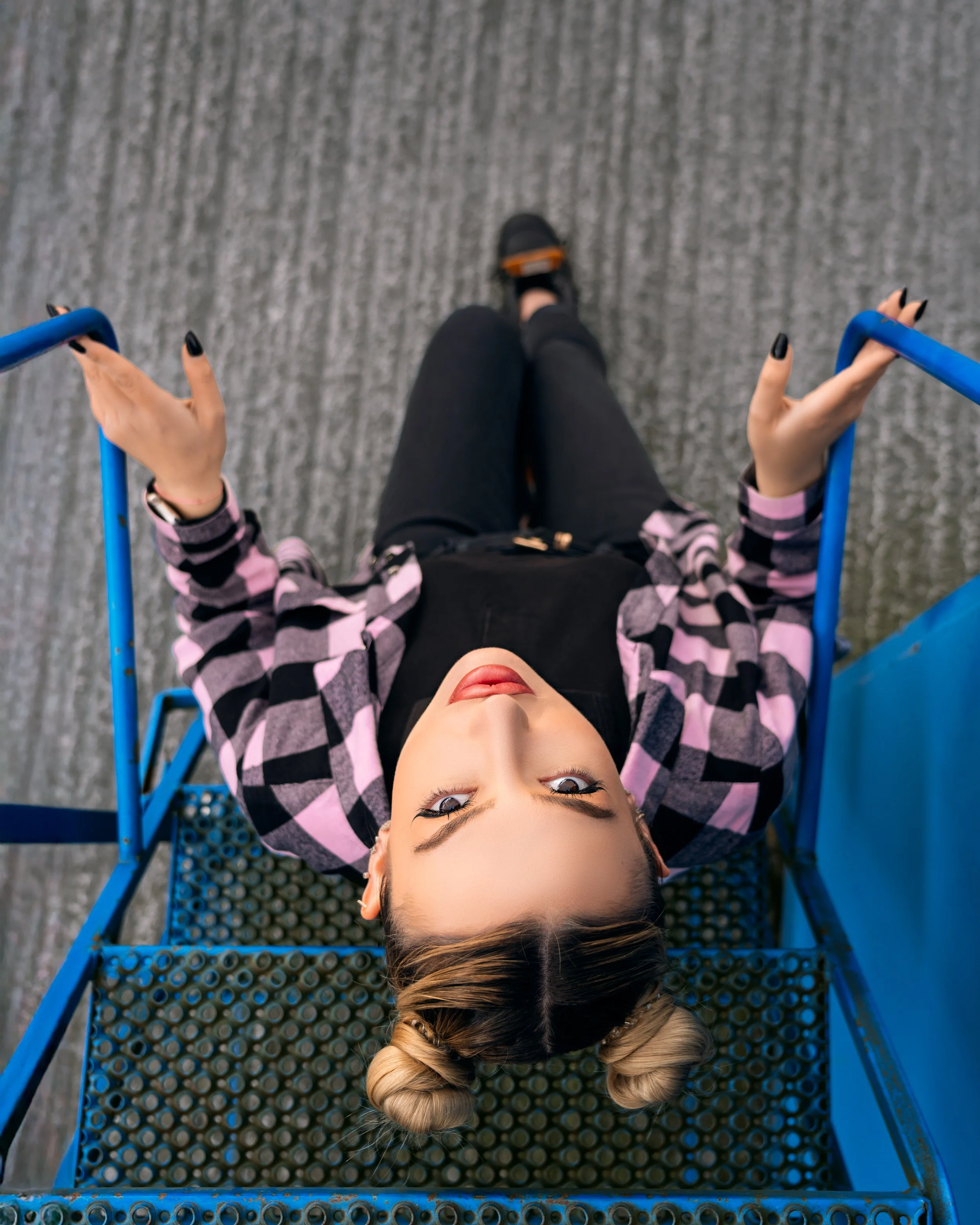 Portla for young girl in black and pink outfit from above seating on a blue metal staircase