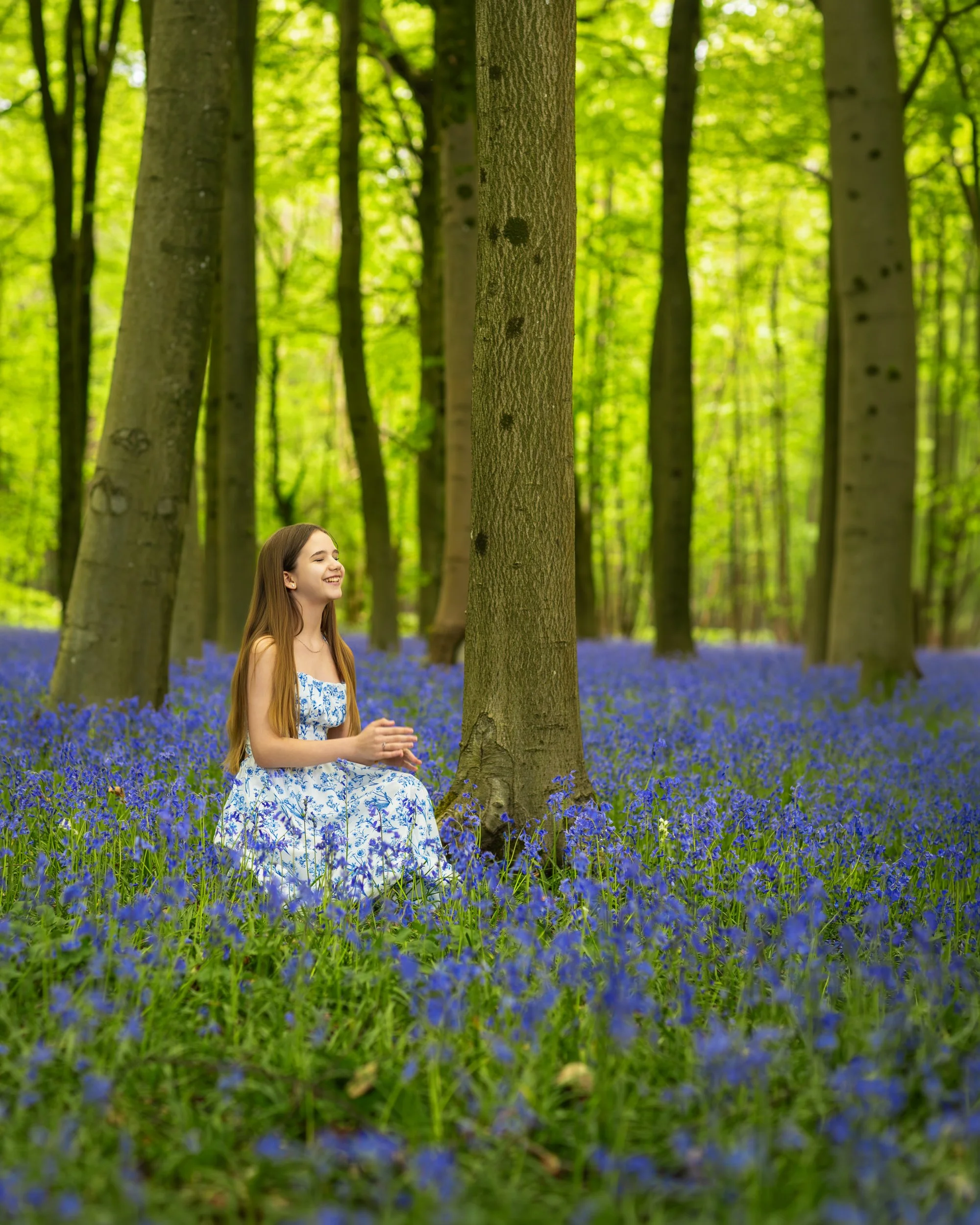A young girl sitting peacefully among blooming bluebells in a quiet woodland, enjoying the calm atmosphere of a bright spring day.