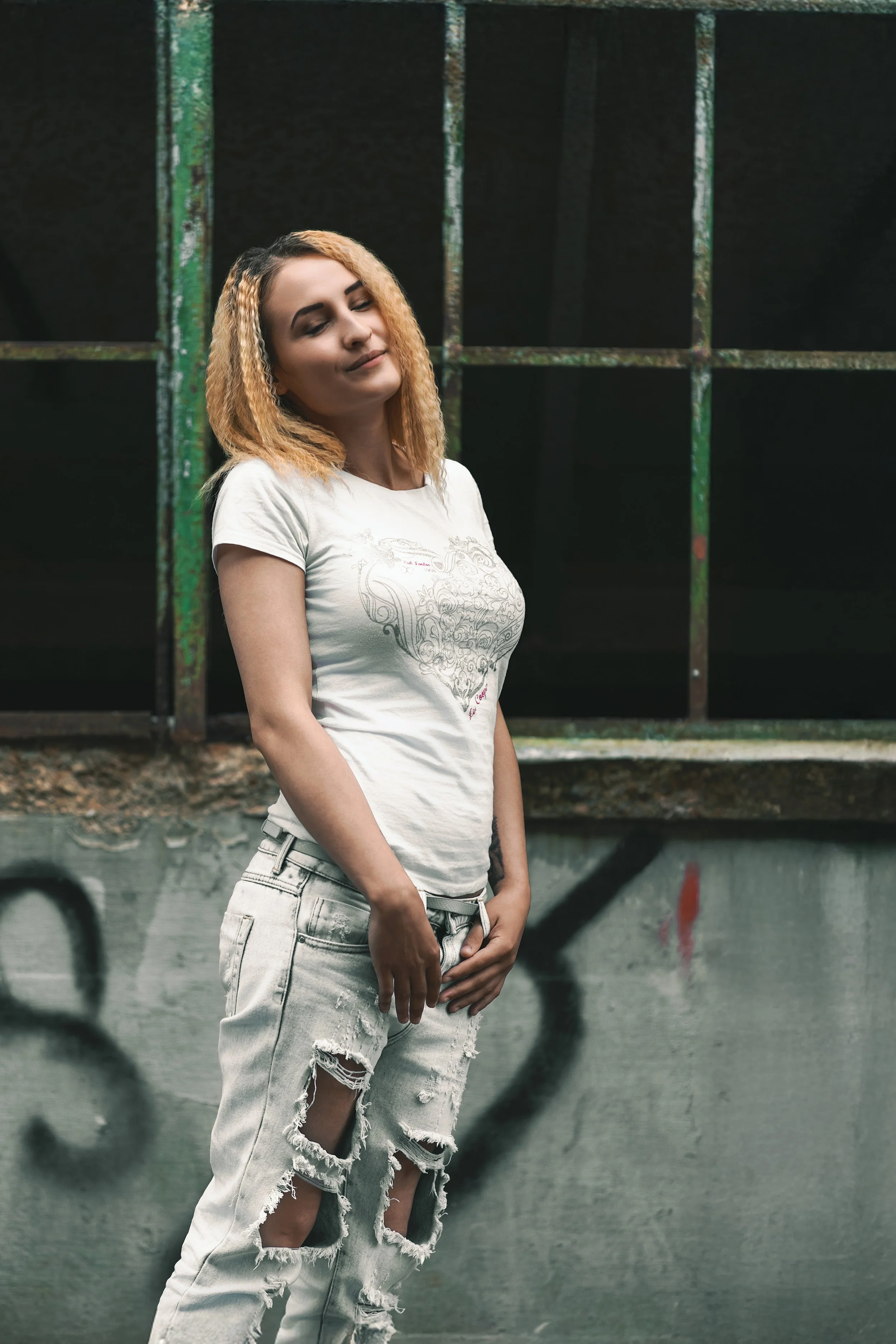Portrait of a young blond woman in white t-shirt and ripped jeans against an industrial background 