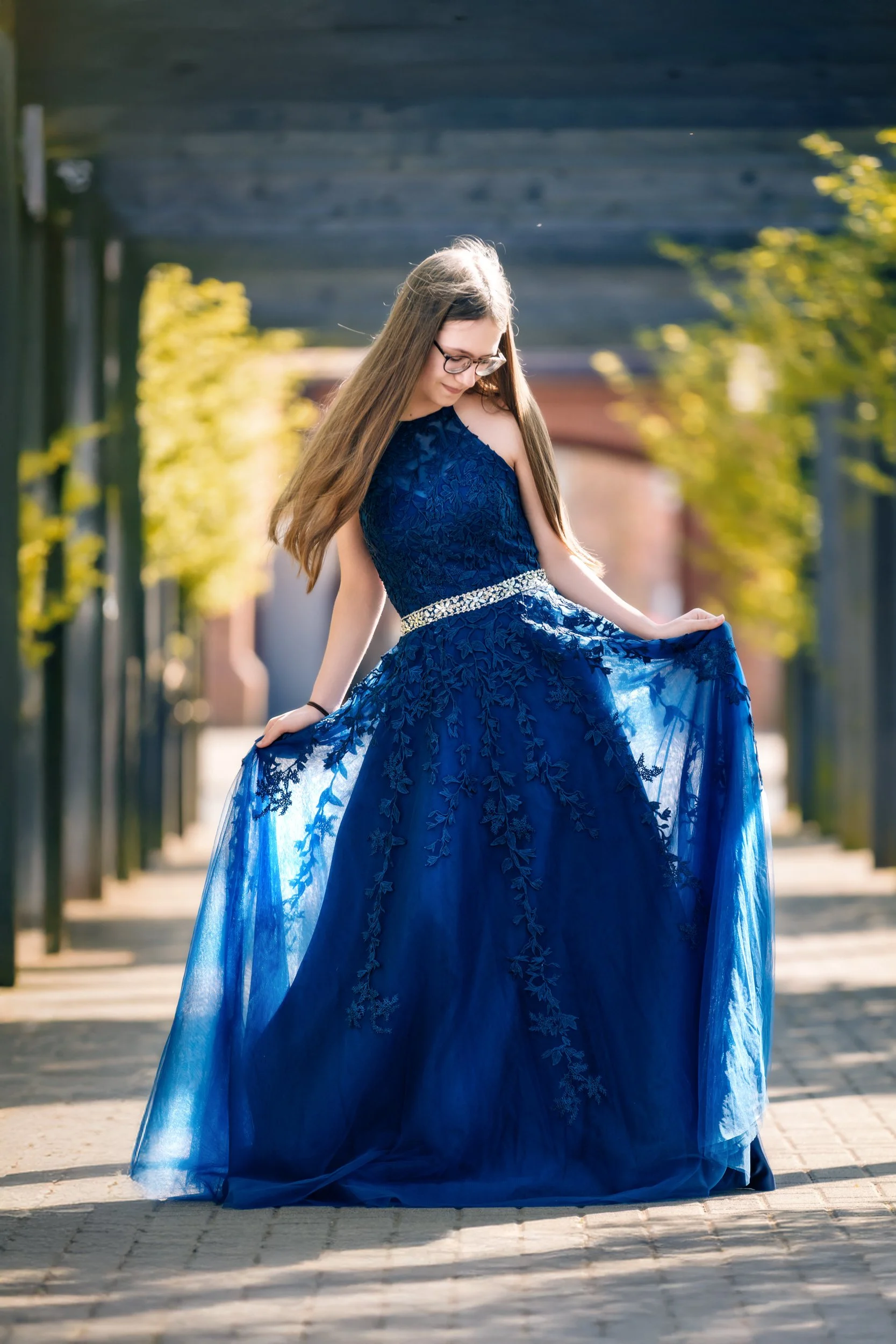 A woman in a flowing blue dress is posing  within an arbour