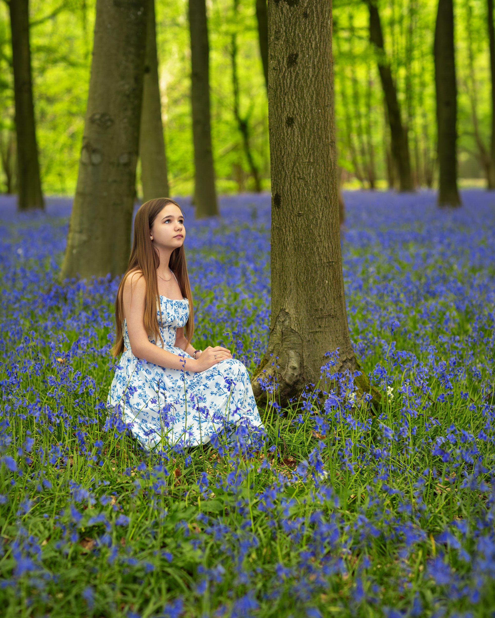 A young girl sitting peacefully among blooming bluebells in a quiet woodland, enjoying the calm atmosphere of a bright spring day.