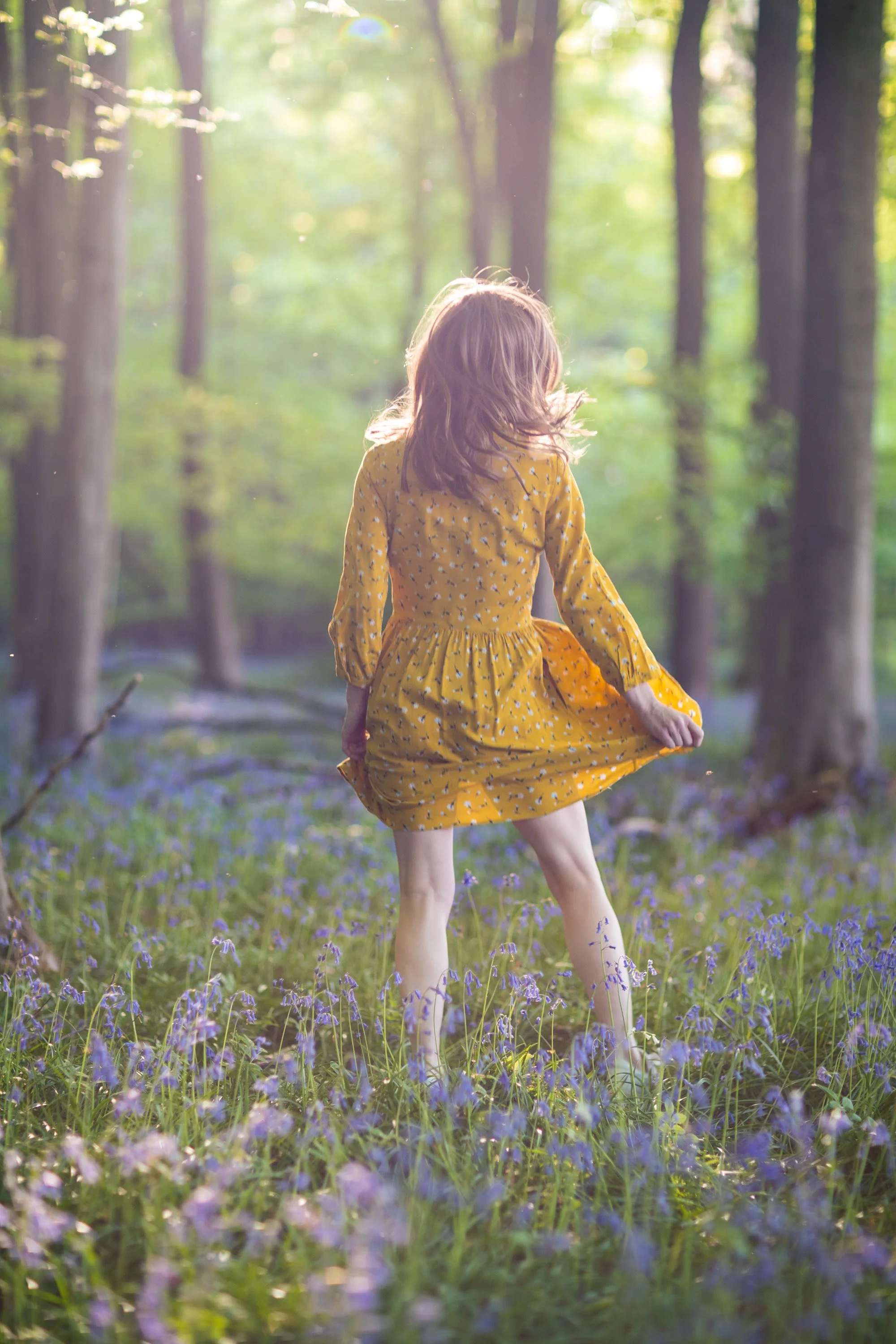 Faceless portrait of a young woman in yellow dress in a forest with the blooming bluebells