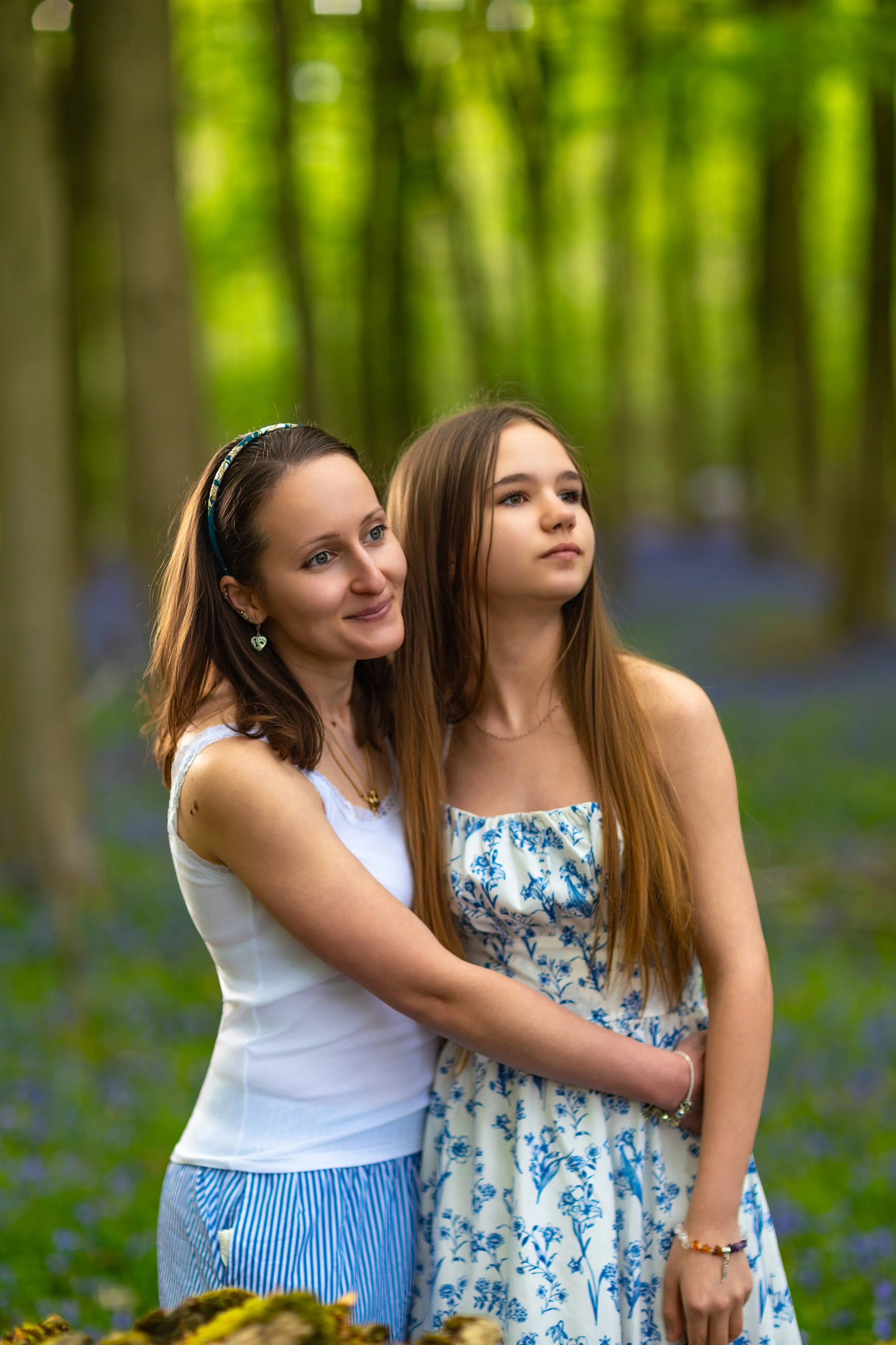 A woman and her niece embracing in a peaceful woodland filled with soft green light and blooming bluebells
