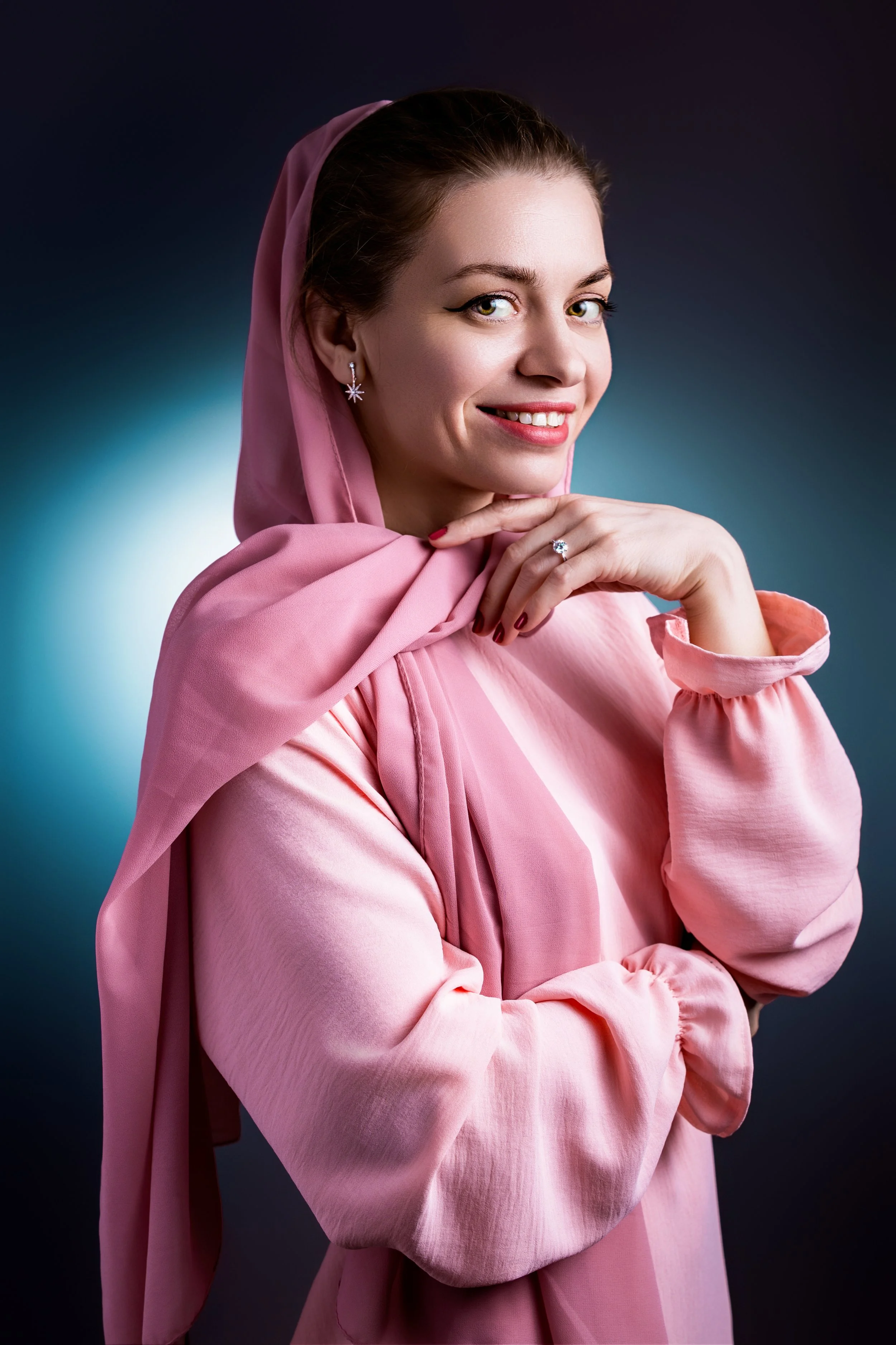 Studio portrait of a young woman wearing a pink dress against a dark to light blue gradient background 