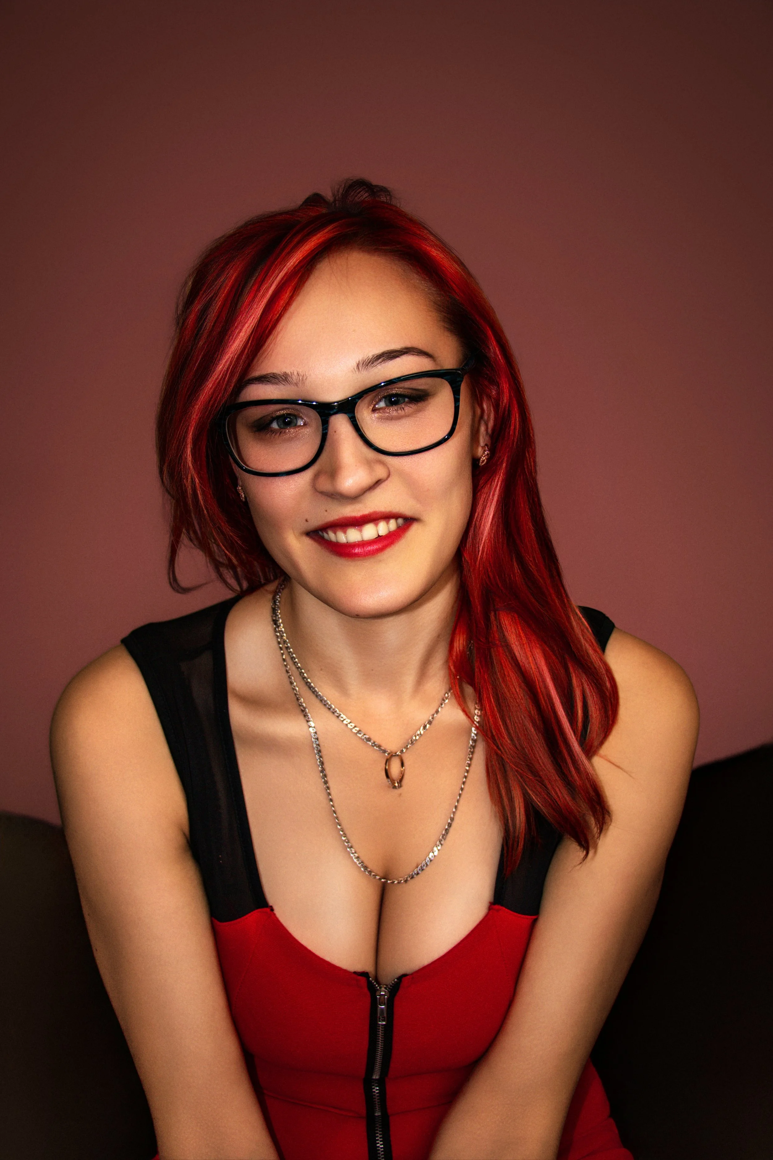 Young red hair girl with red lips in red dress sitting in front of a red background