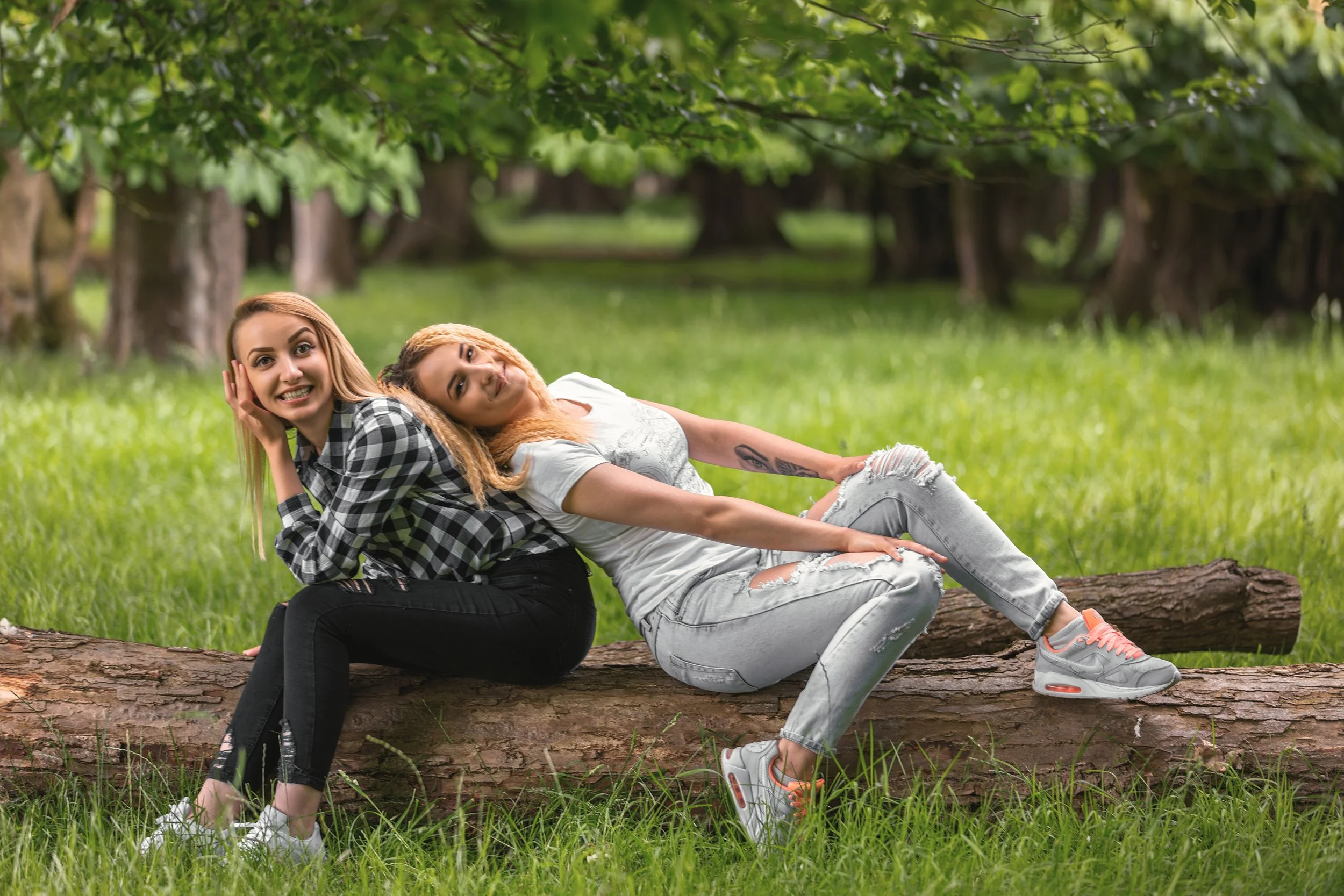 Portrait to two young blonde girls sitting on a tree trunk in the spring Forest