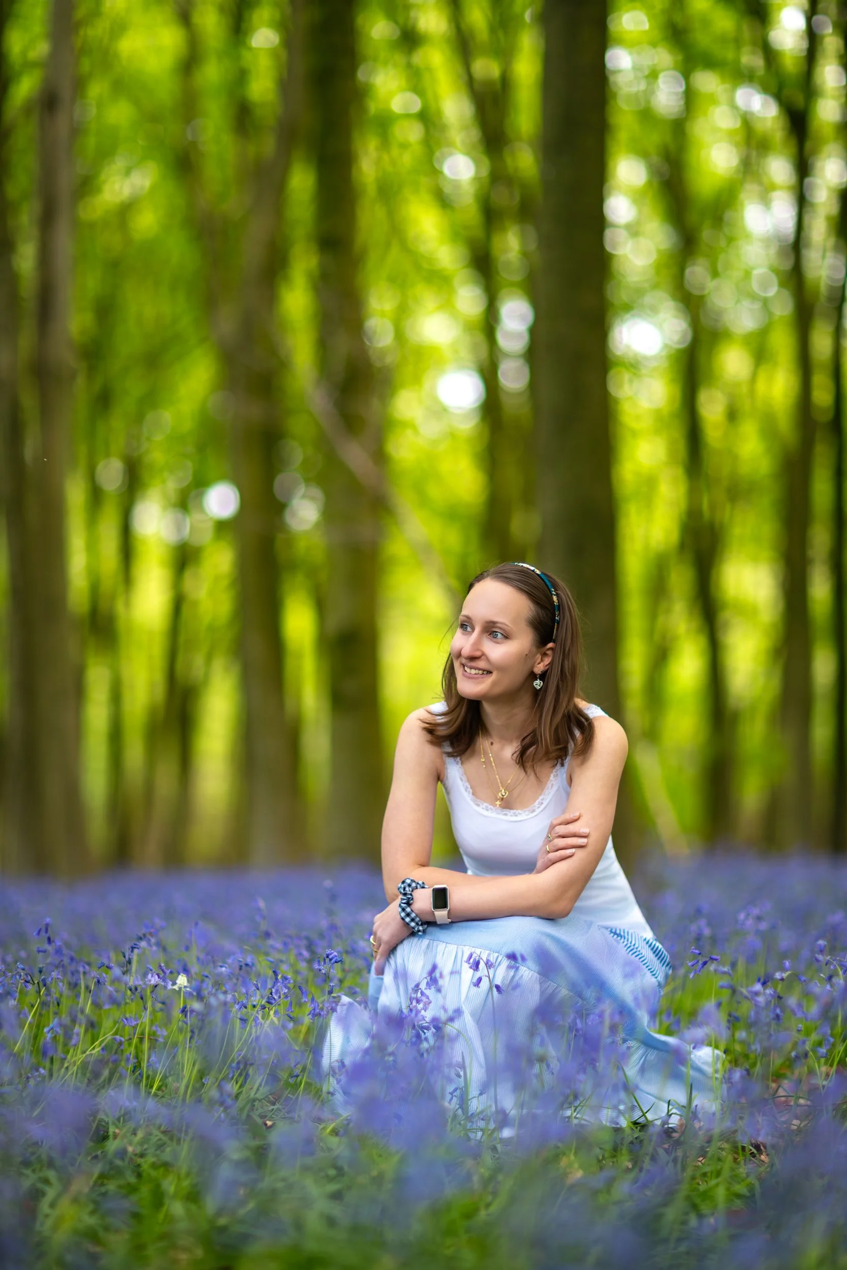 A woman sitting among blooming bluebells in a tranquil woodland, surrounded by soft green light and the peaceful atmosphere of spring.
