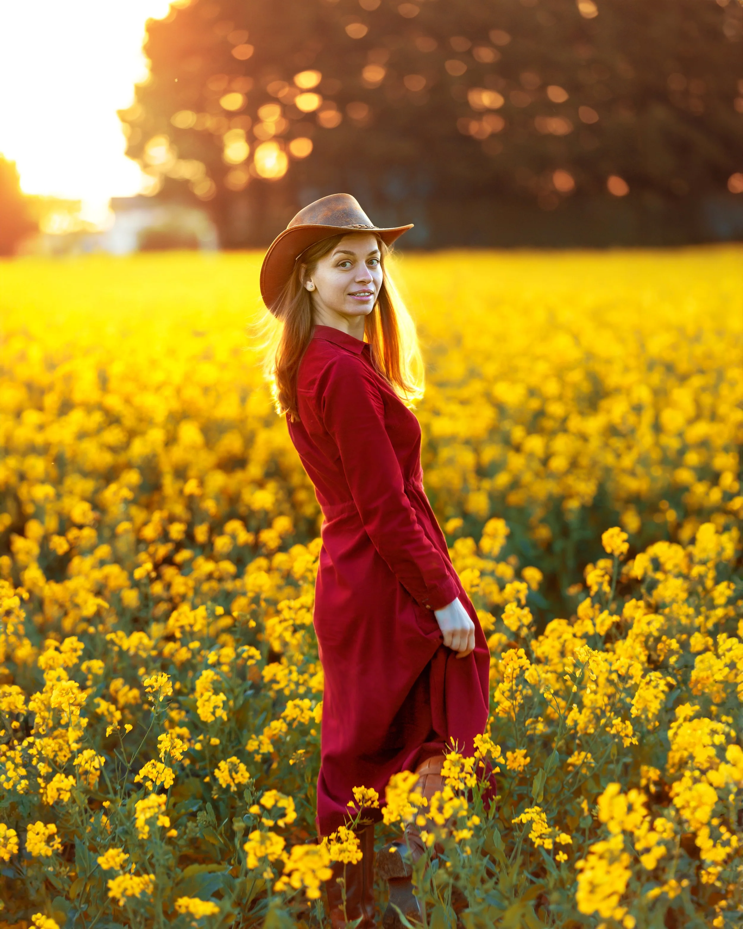 Portrait of a woman on a rape seed field, wearing a Red Dress and a cowboy hat in the sunset