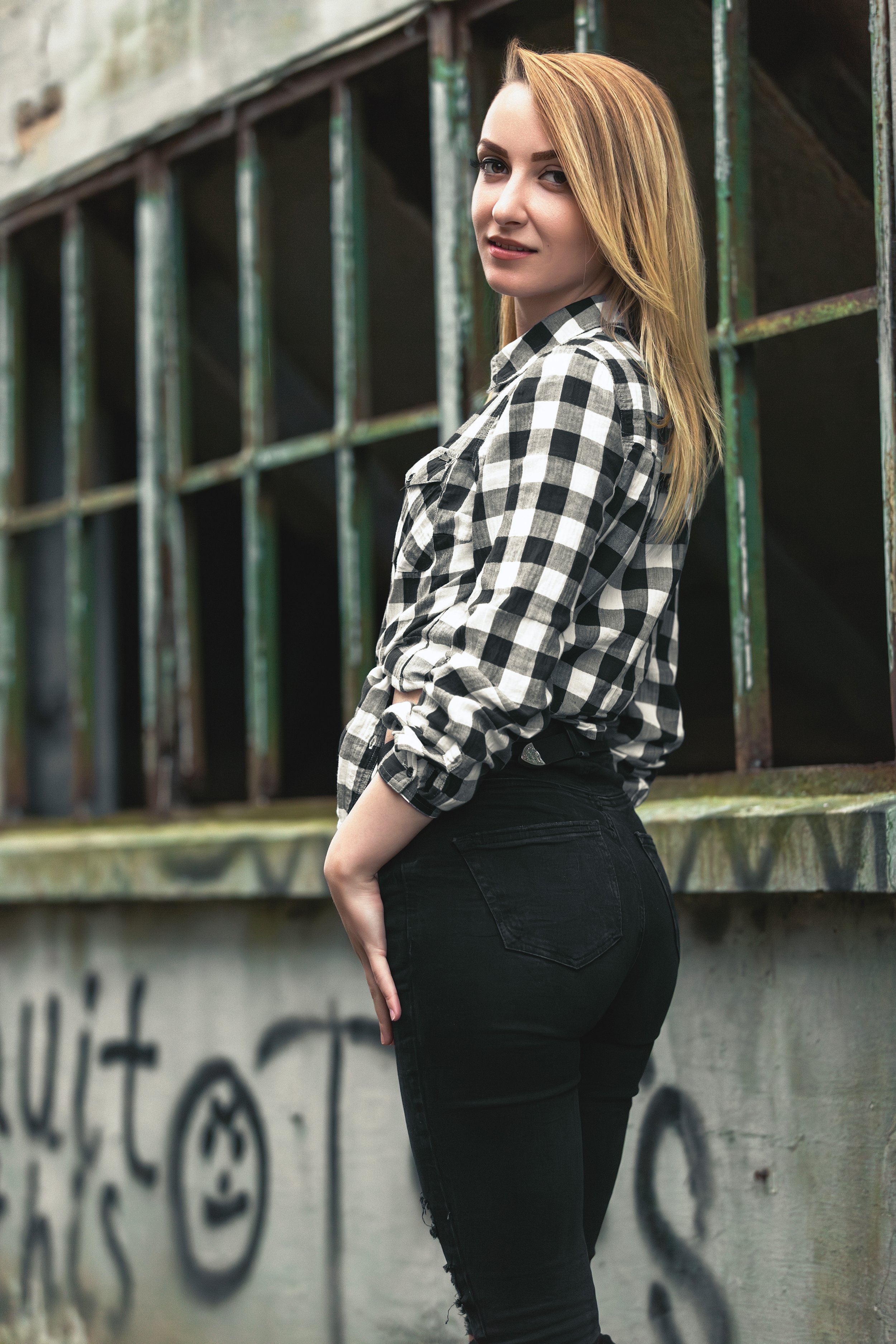 Portrait of a young confident woman in an industrial estate in front of an old concrete building covered in graffiti and all the windows missing only their rusty green metal frame remained 