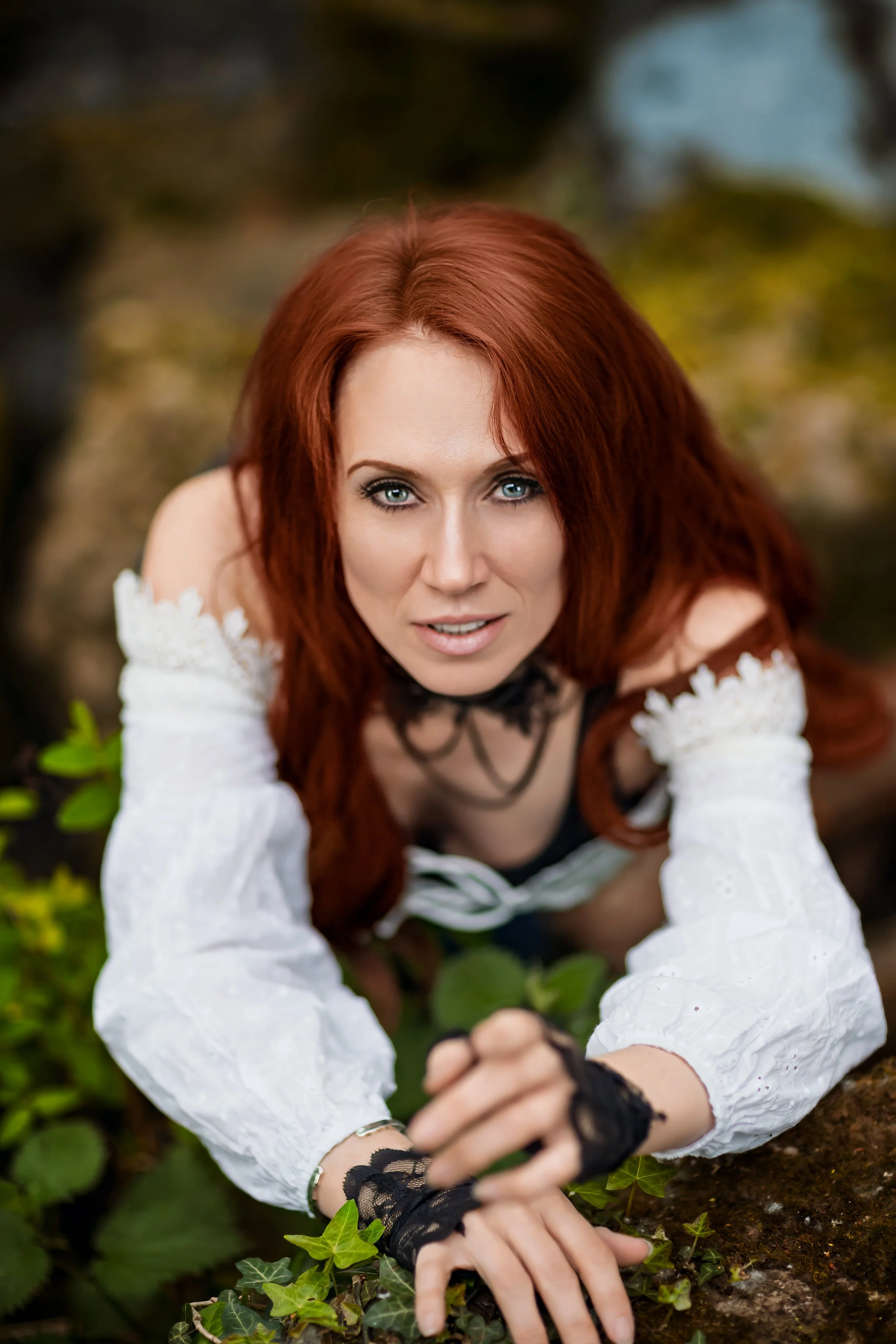 Stylised portrait of a red haired woman wearing vintage white corset and lace gloves by a waterfall in Cheltenham 