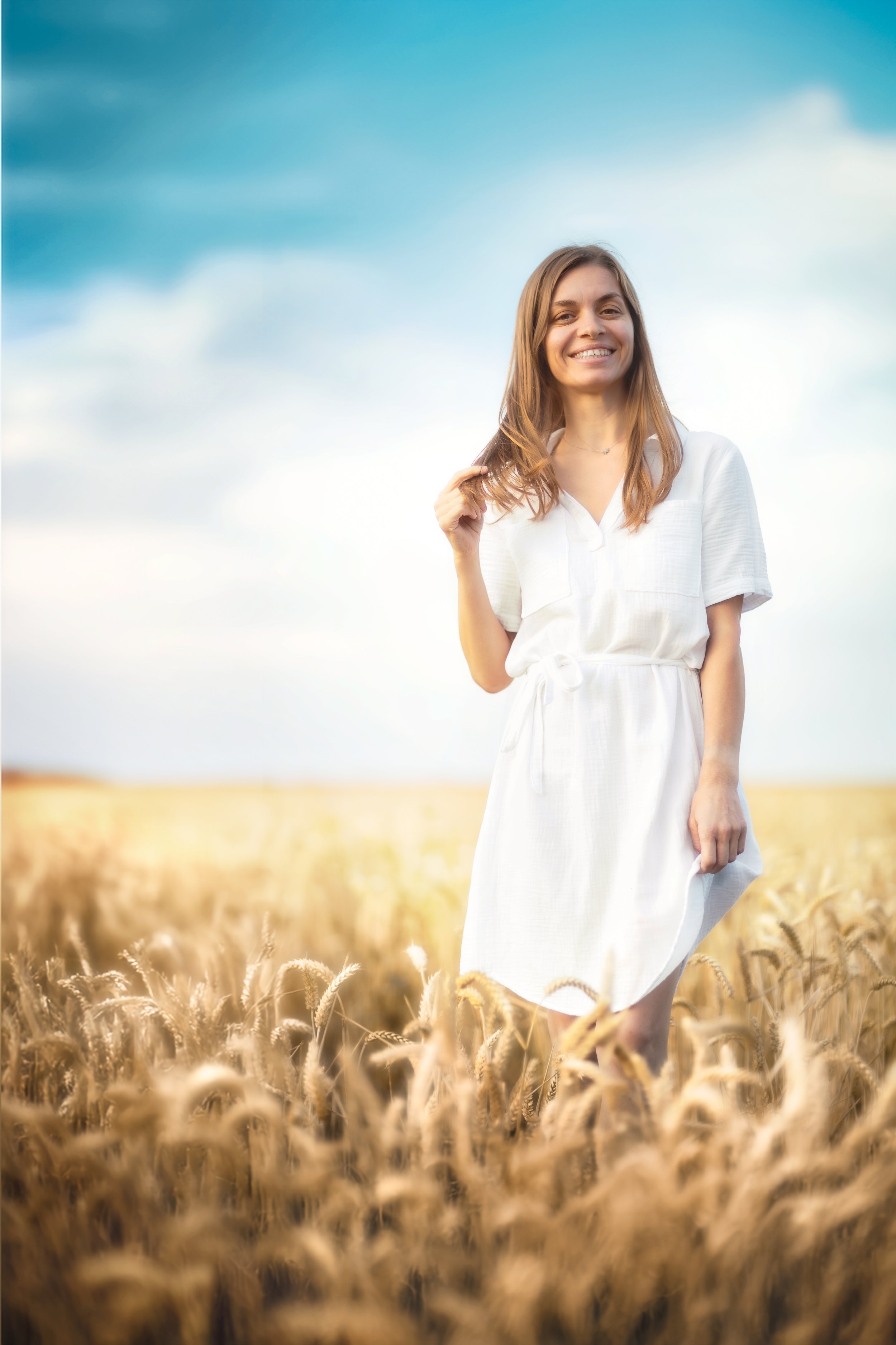Portrait of a happy woman on a wheat field wearing white summer dress 