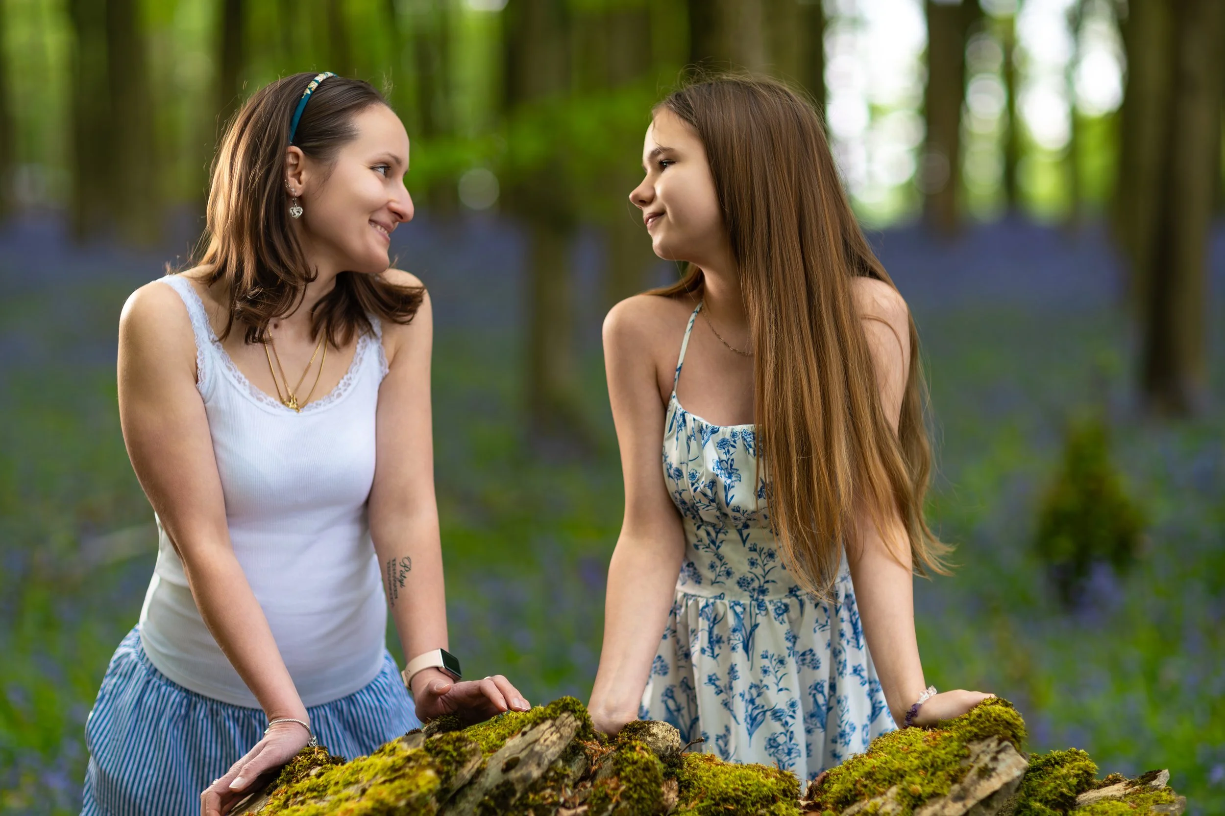 A woman and her niece sharing a quiet moment together beside a moss-covered stone wall in a tranquil forest setting.