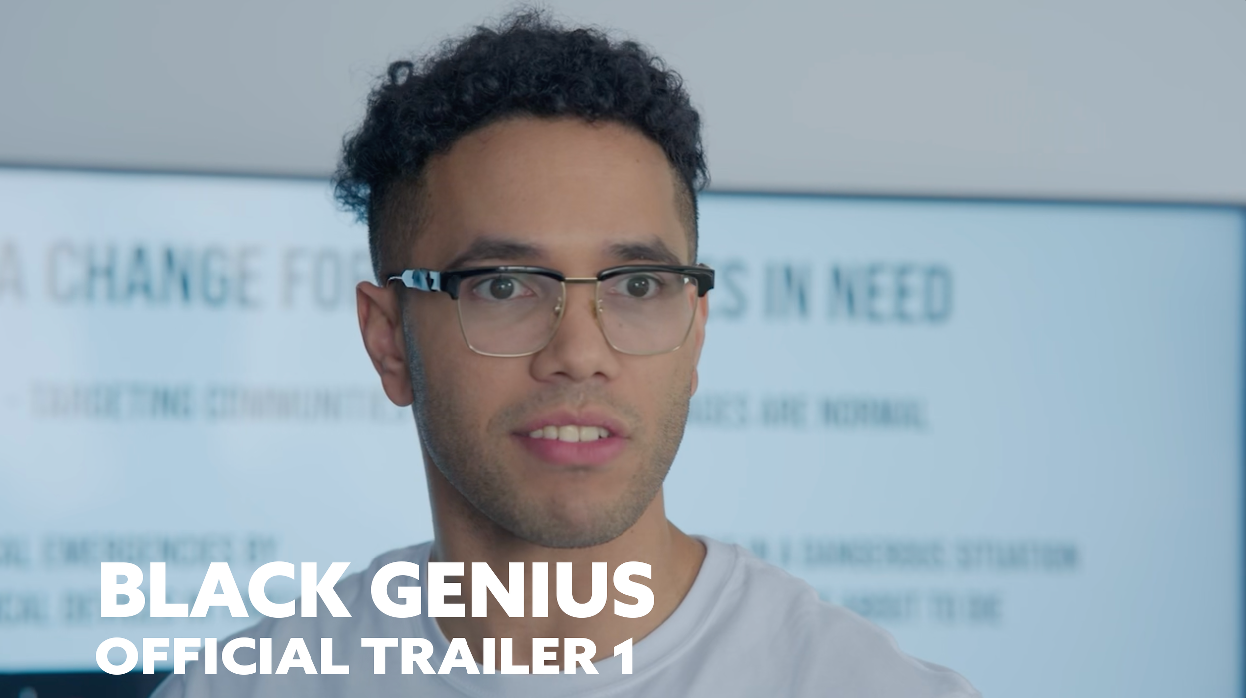 A young man with short curly dark hair and glasses, looking at the camera with a neutral expression, in front of a blurred background with text, and the words 'BLACK GENIUS OFFICIAL TRAILER 1' overlayed at the bottom.