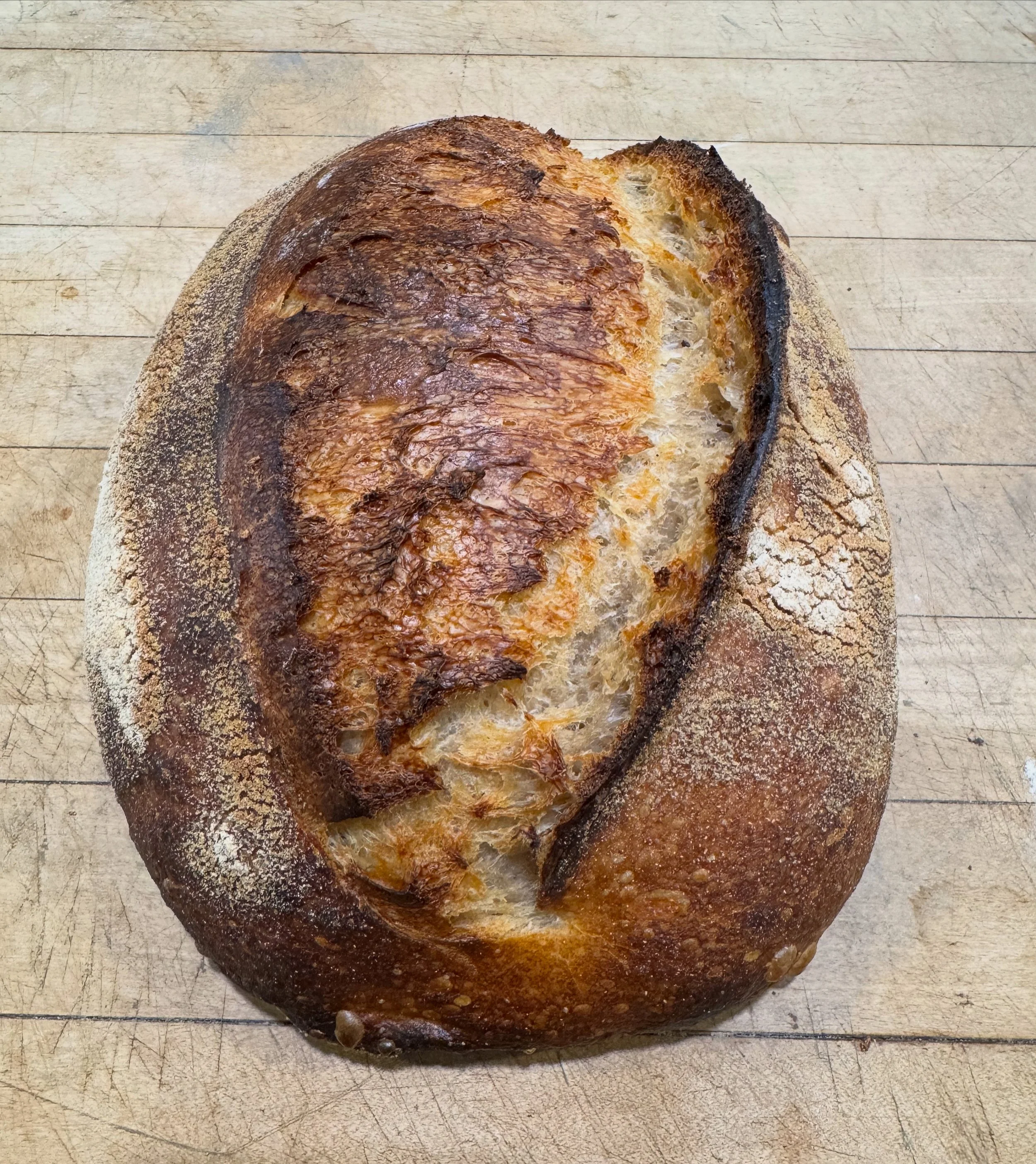 Baked loaf of bread with a golden-brown crust on a wooden surface.