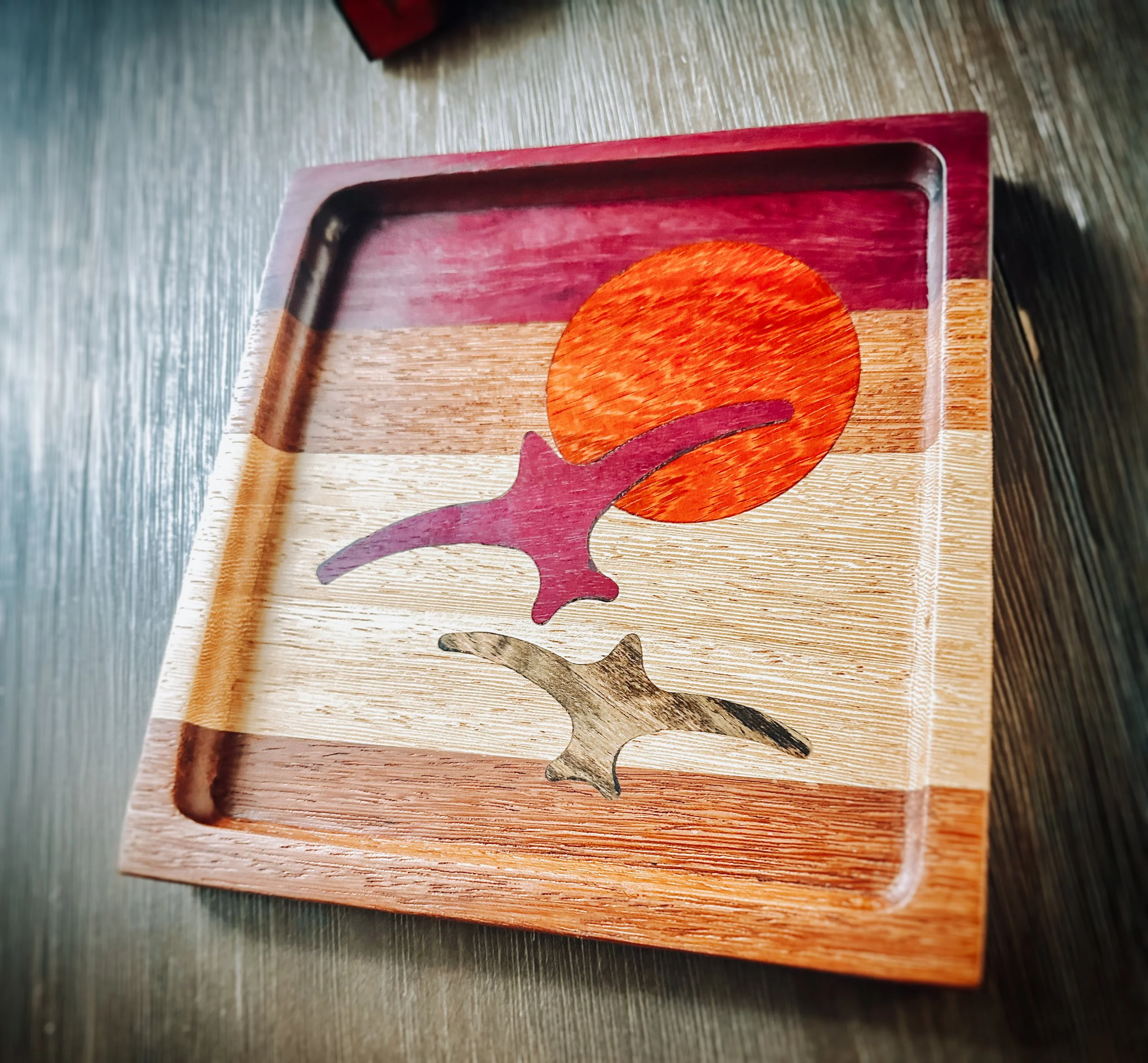 A wooden tray with a painted sunset, a pink bird, and a small beige bird illustration.
