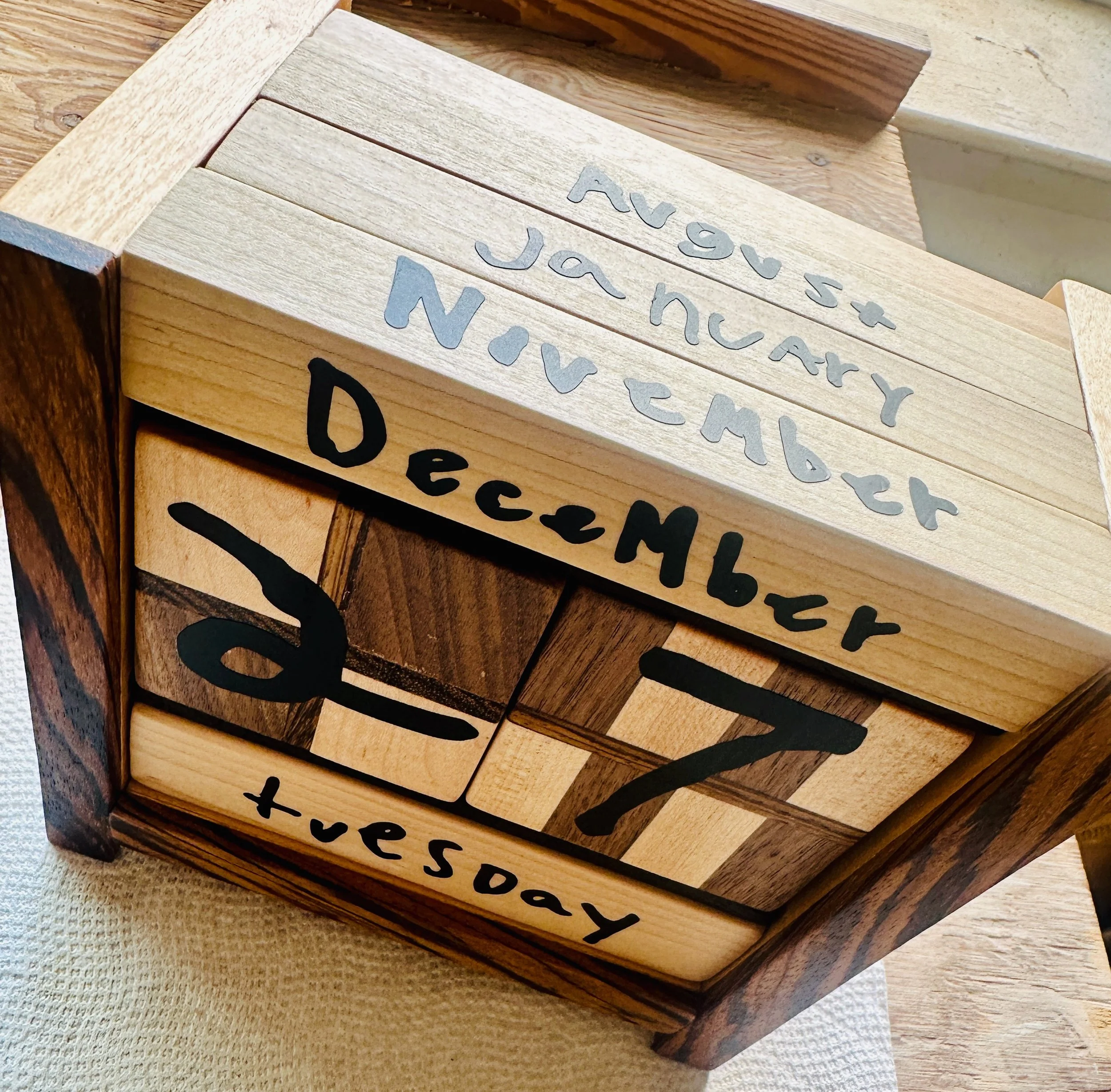 Wooden blocks with inspirational text, including a calendar date, the words "DECEMBER 3rd," and the phrase "tues day" on a piece of furniture.