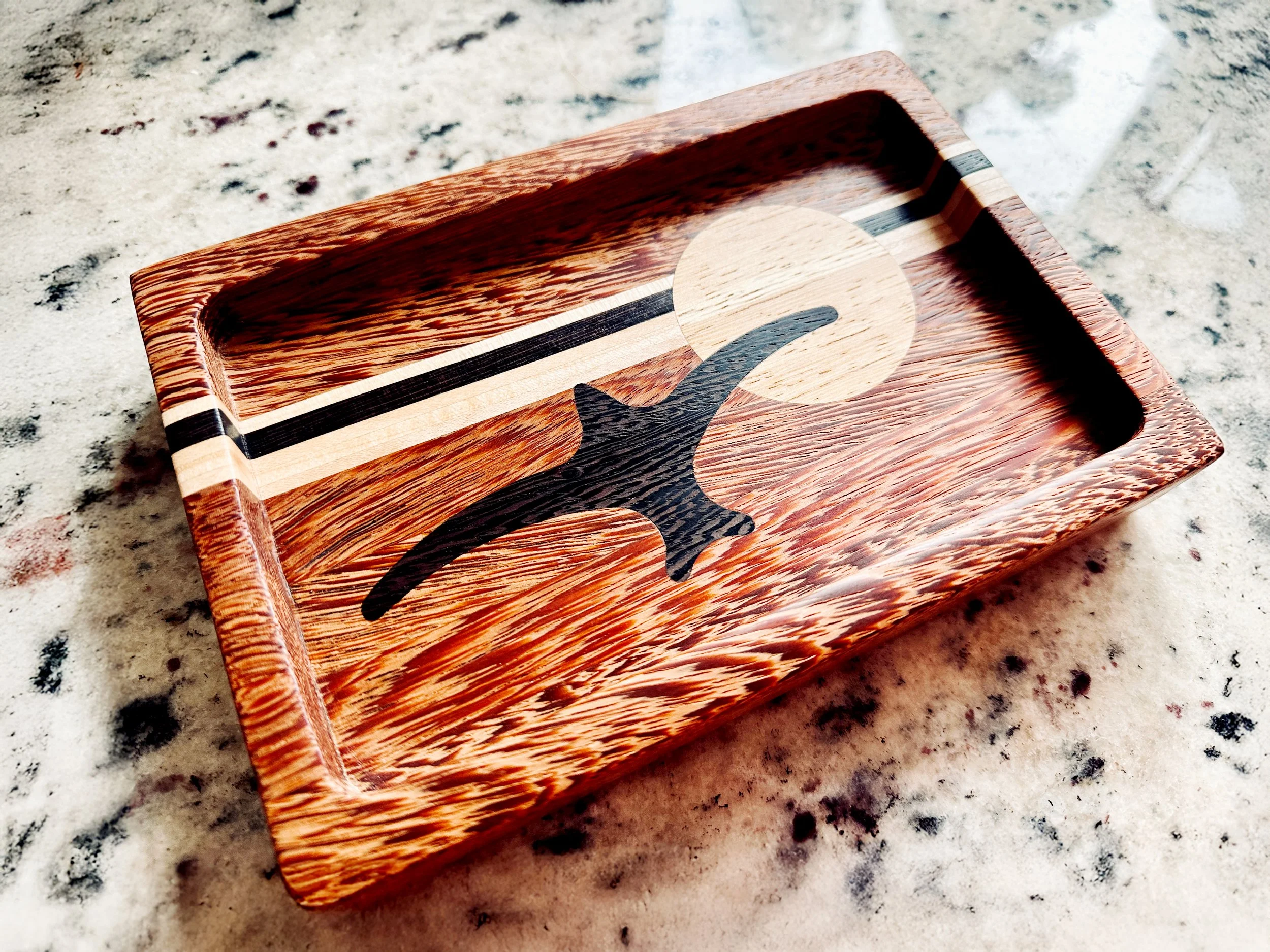 Wooden tray with a black and beige abstract design, resting on a marble surface.