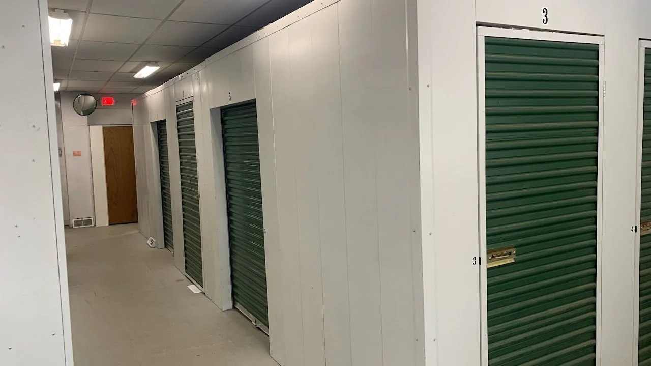 Indoor storage facility with green roll-up doors and a wooden door at the end of the hallway.