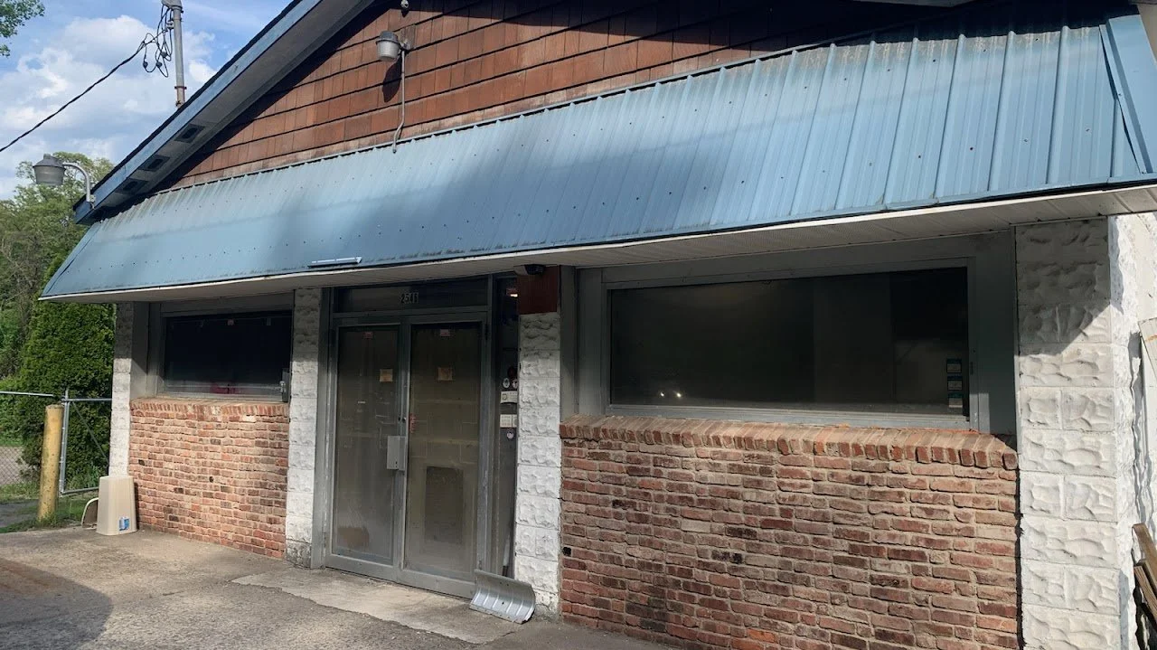 Front view of a building with brick and stone exterior, featuring a metal awning, glass double doors, and large windows.