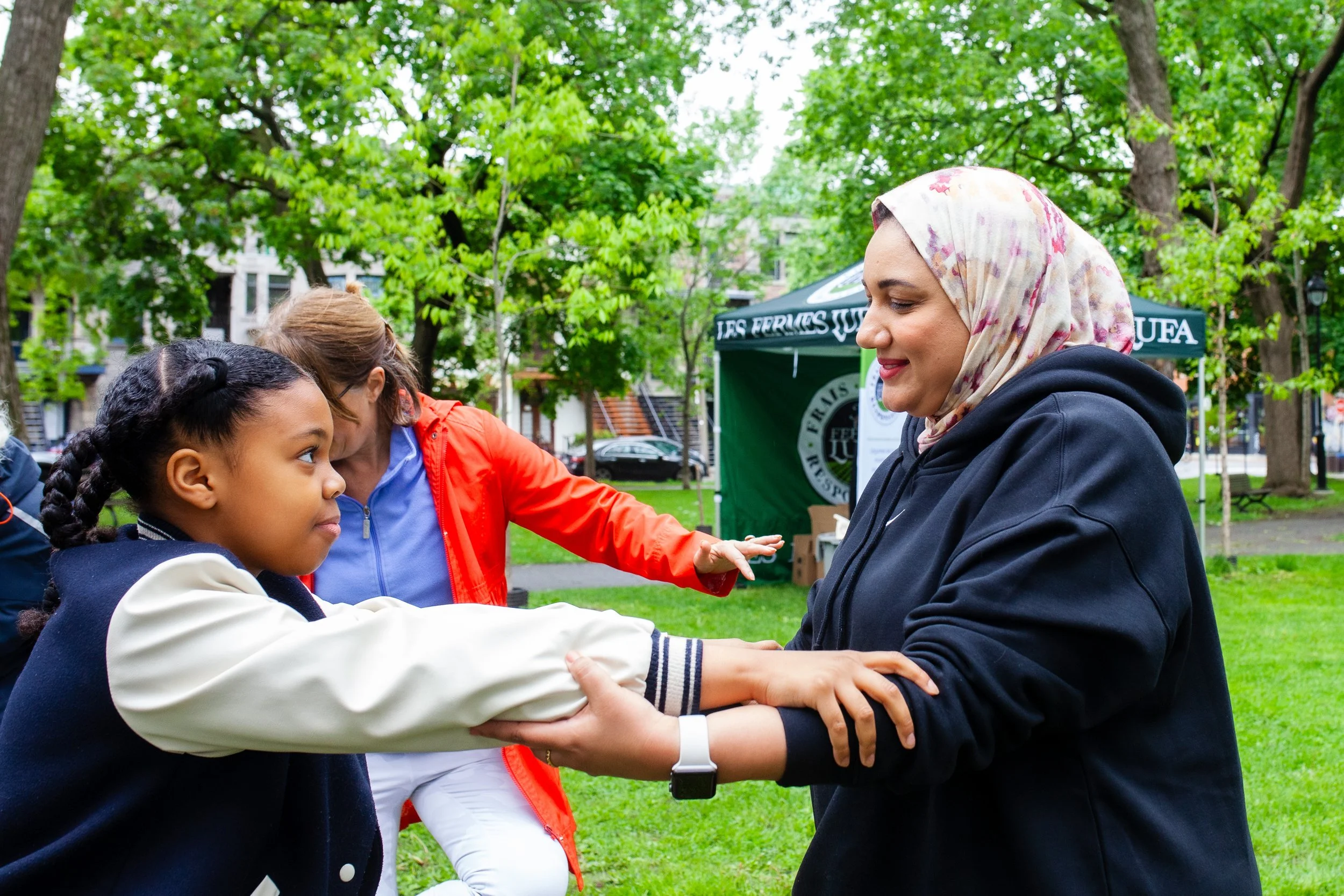Une femme portant un foulard coloré aidant une jeune fille à faire une activité dans un parc lors d'un événement en plein air.